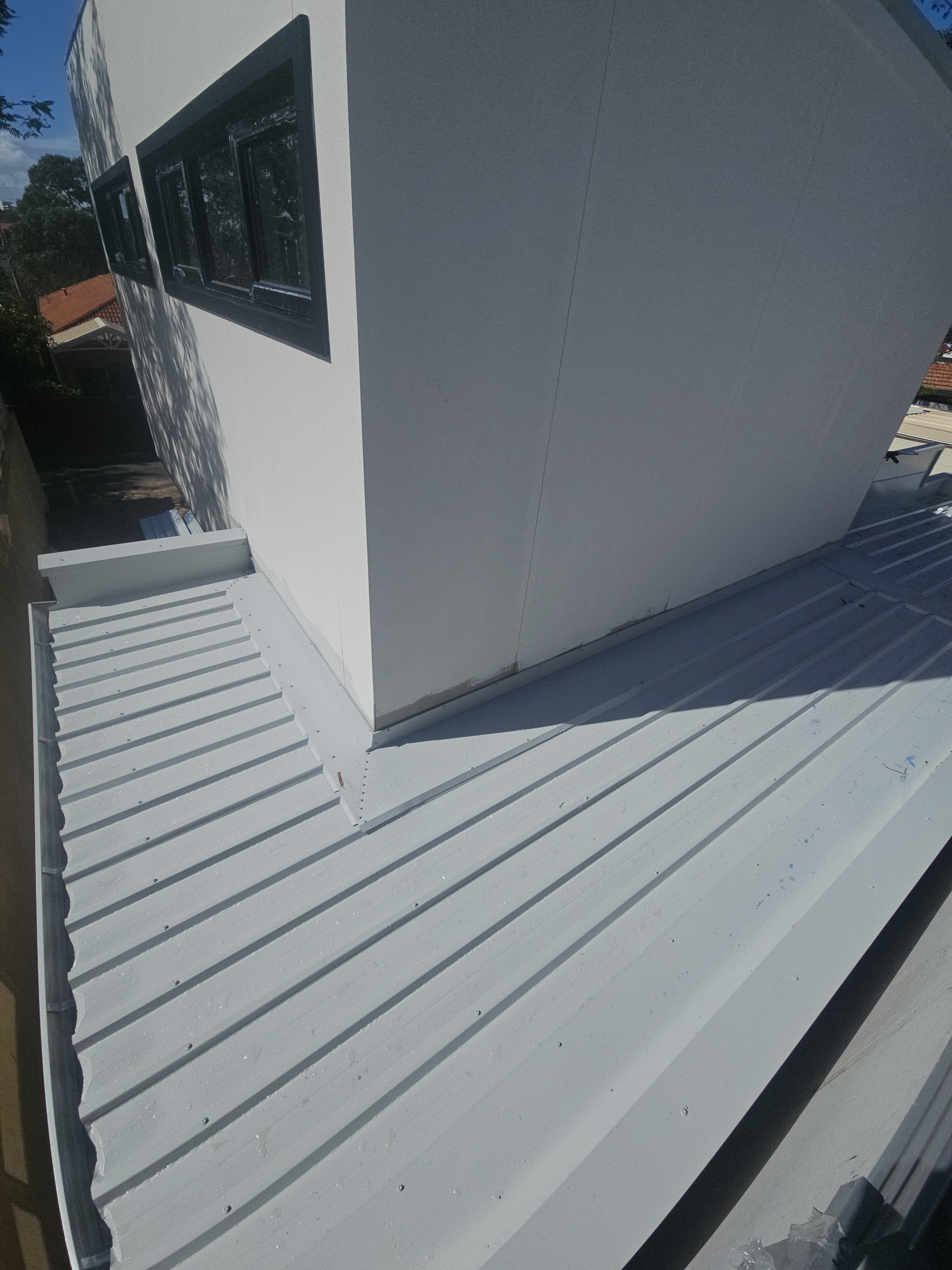 Roof and exterior wall of a modern building with white siding and black window frames, viewed from above.