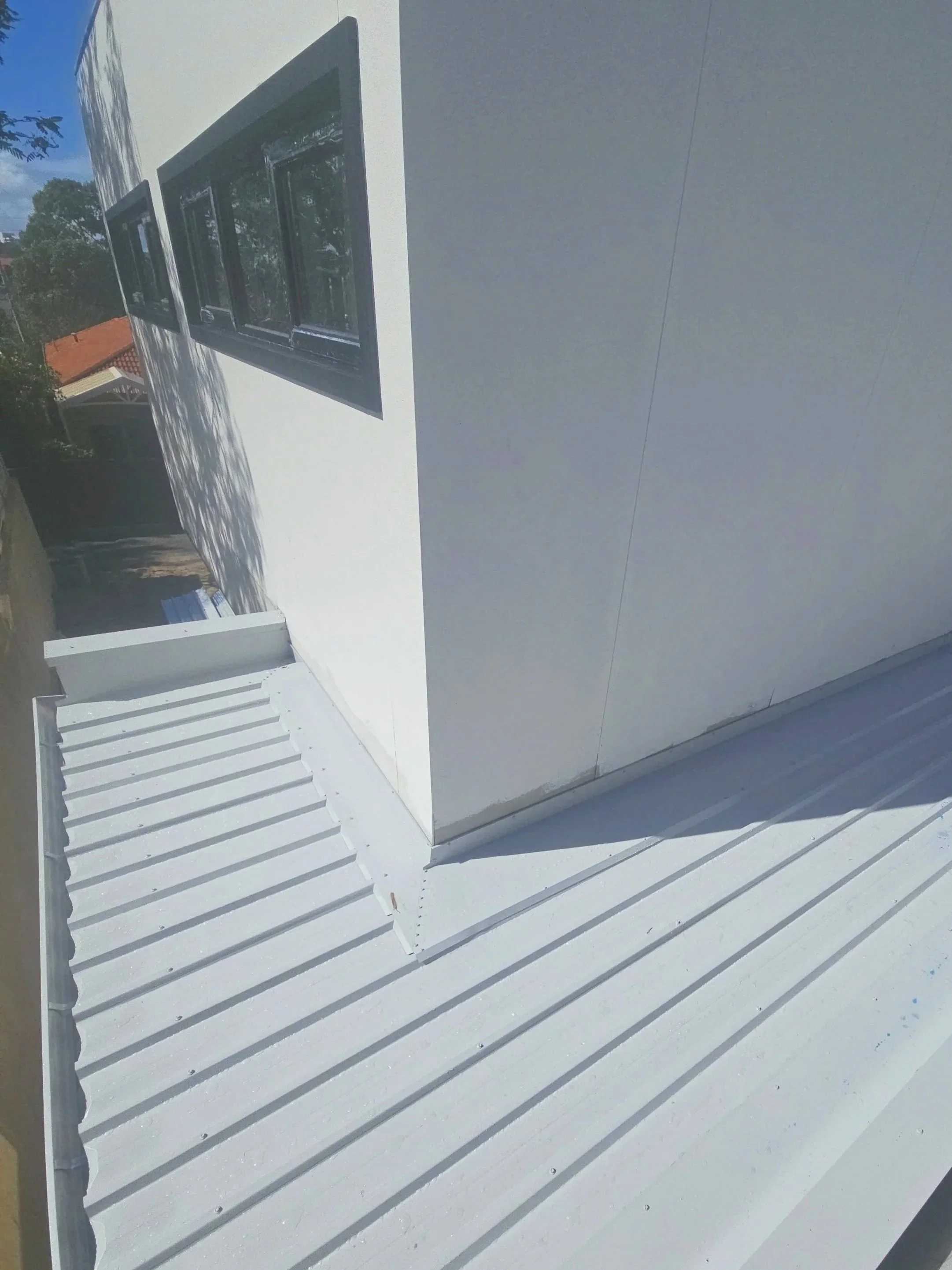 Photo of a building's exterior corner with three black windows and a flat metal roof with all white paint.