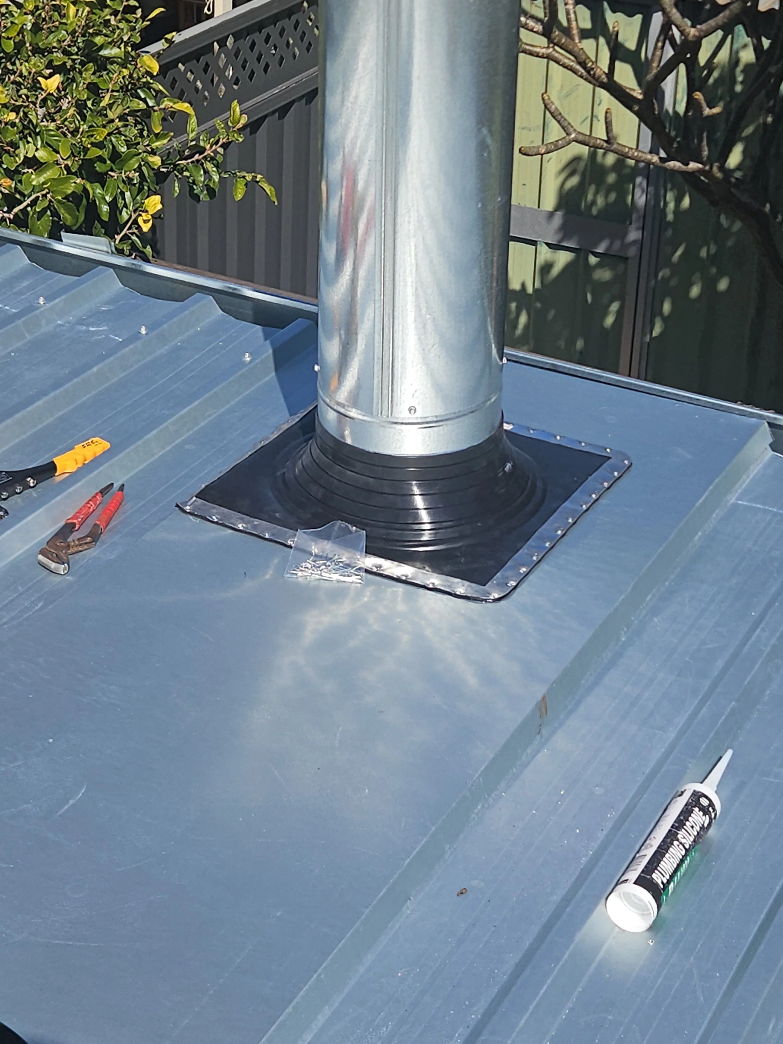Metal roof with a chimney flashing being installed, tools and sealant tube on the roof.