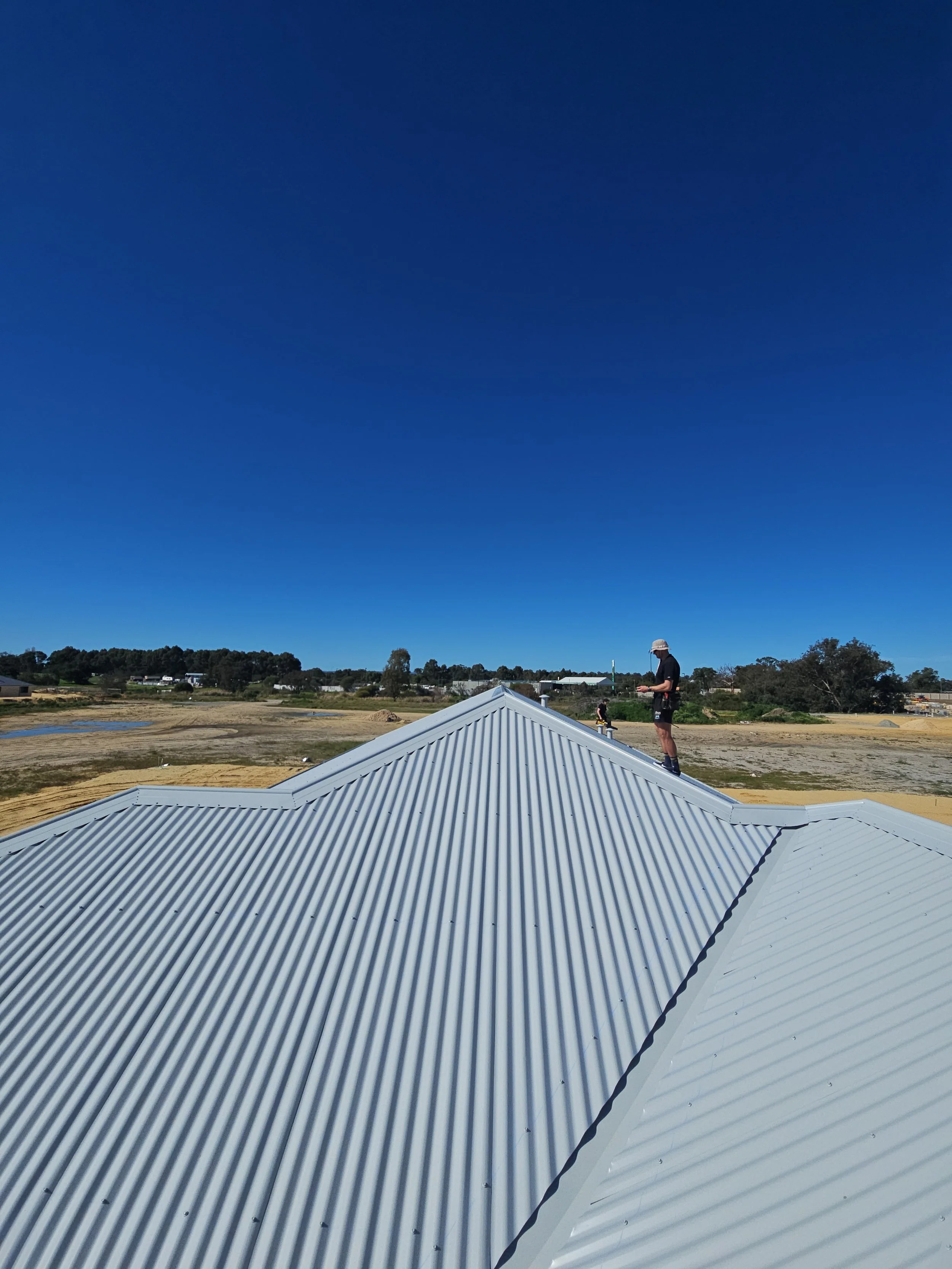 Person standing on a corrugated metal roof under a clear blue sky in a rural area.