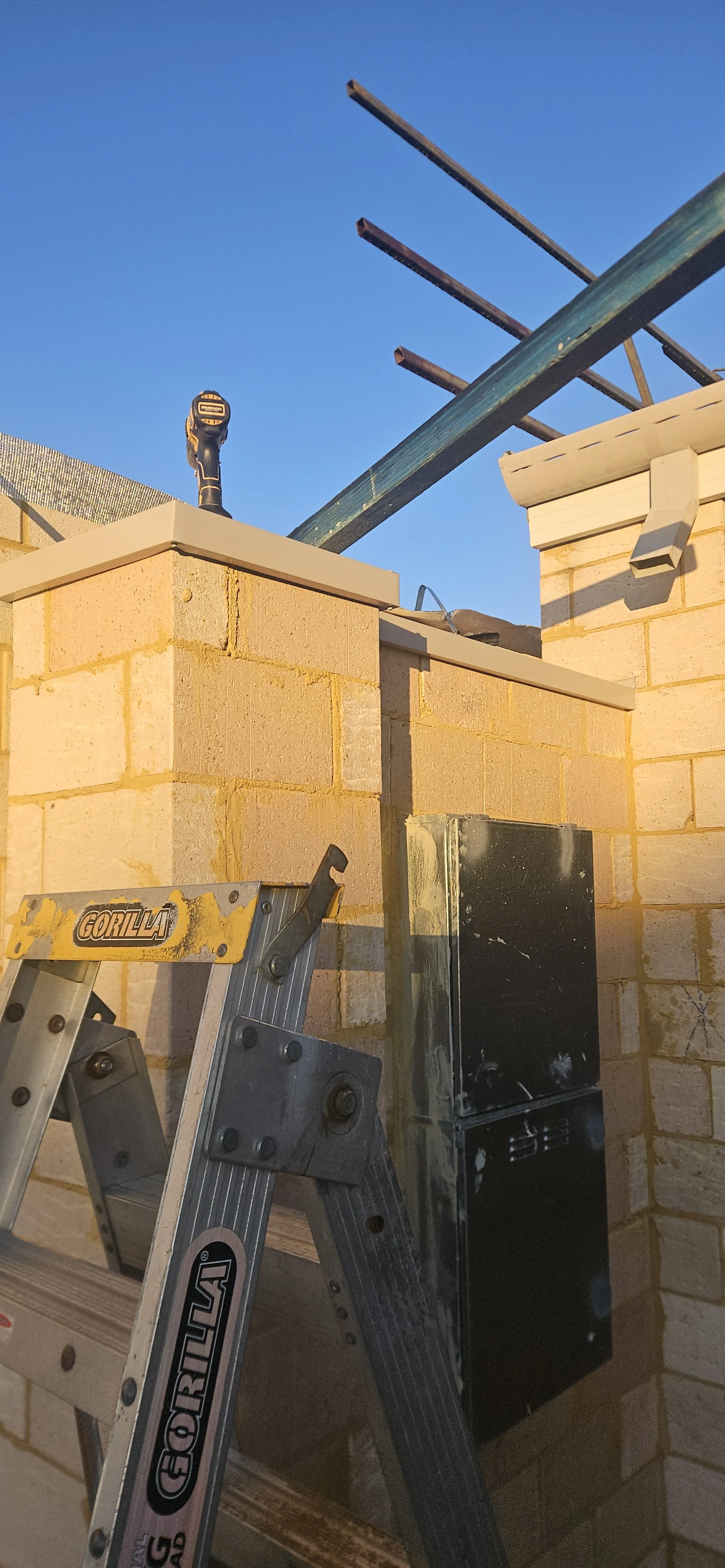 Construction site with brick wall, a step ladder, and metal beams against a clear blue sky.