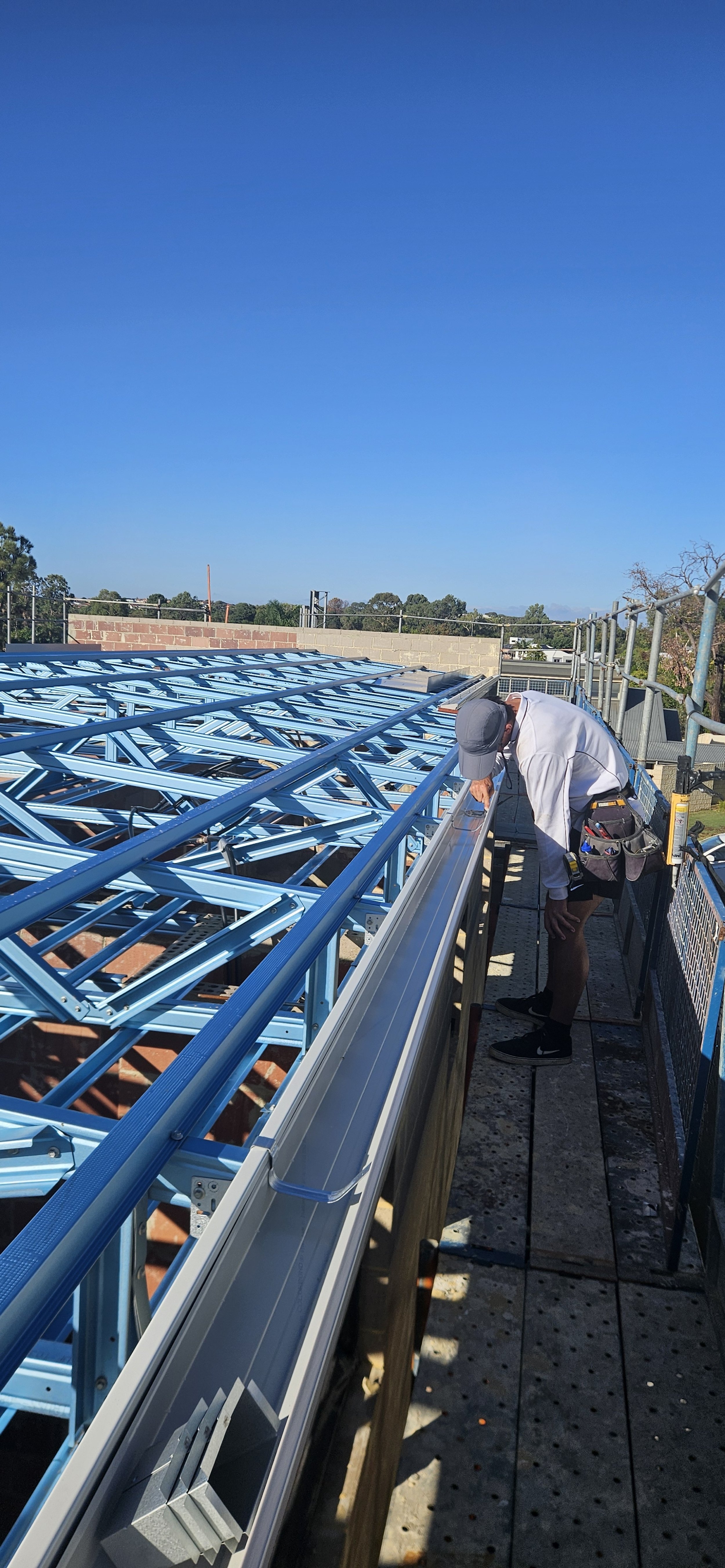A construction worker installing solar panels on a roof under a clear blue sky.