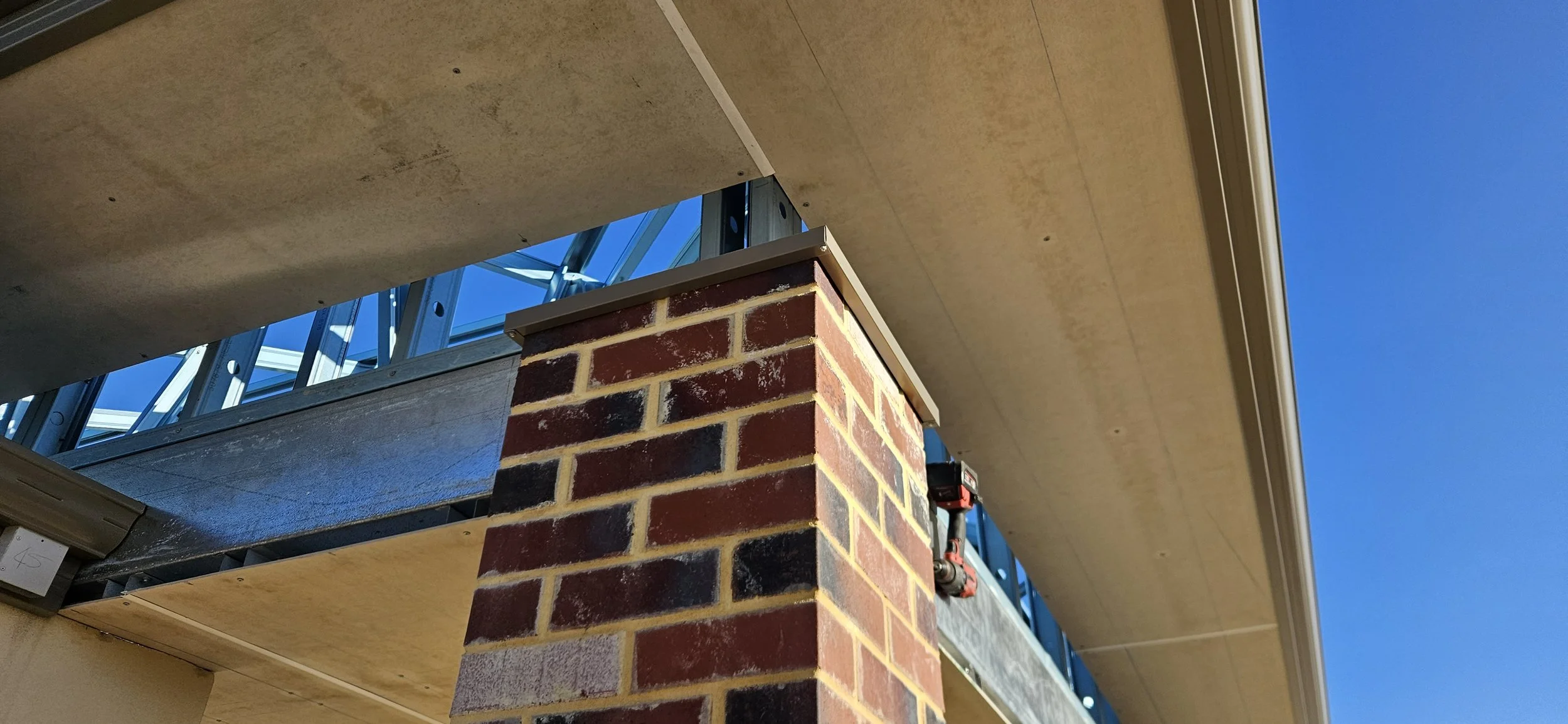 Under construction building with exposed brick column, framing, and roof under blue sky.