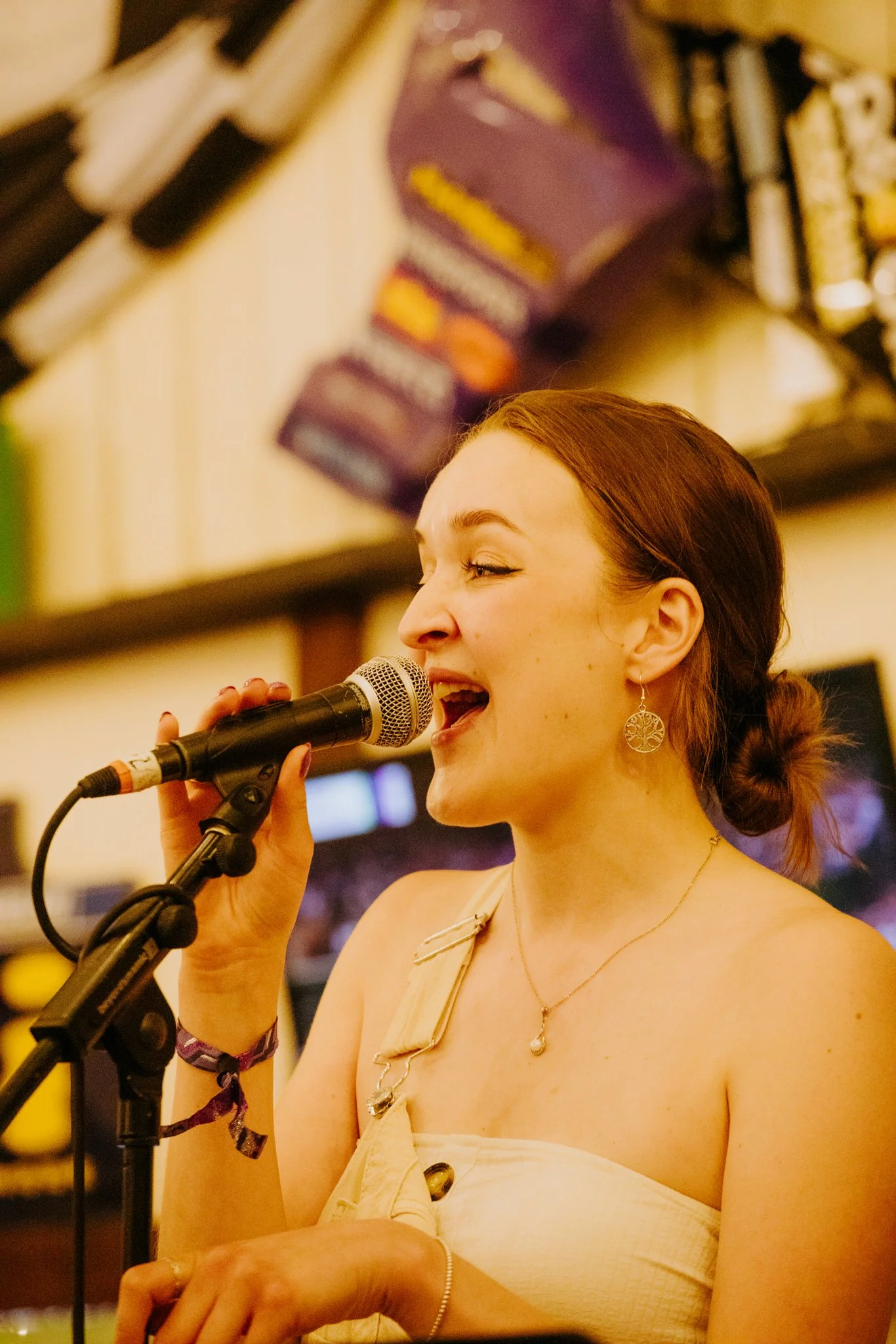 Woman singing into a microphone, wearing circular earrings and a strapless top, with a colorful background.