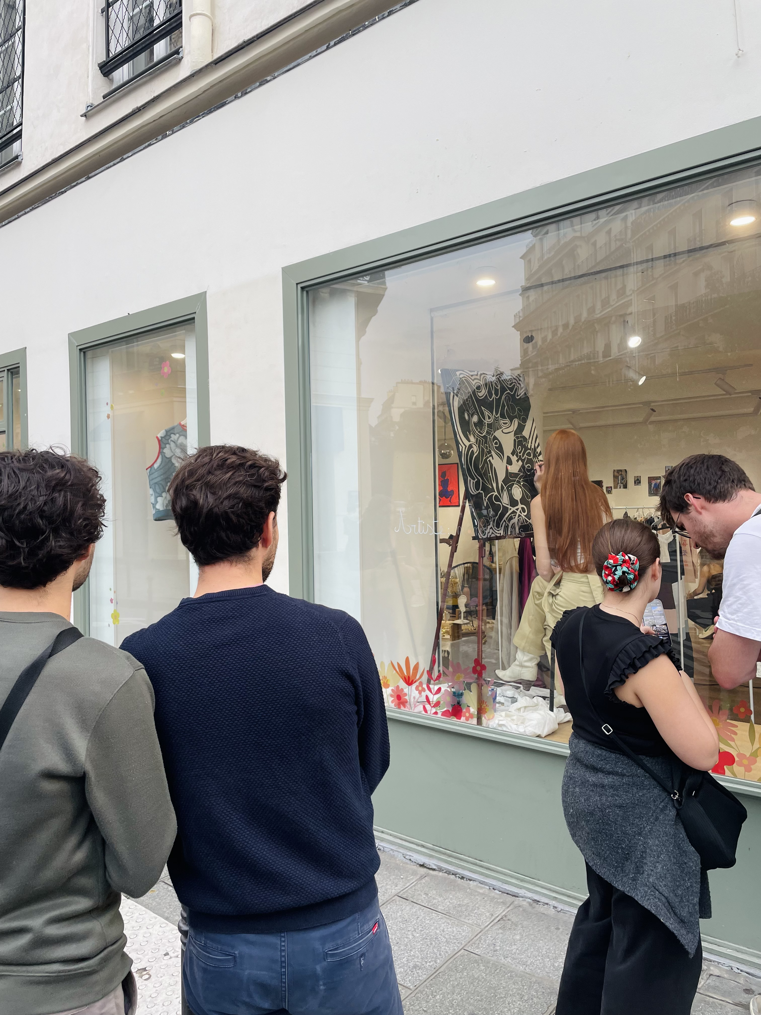 Groupe de personnes regardant de dehors, l'artiste peintre Manon SAJOUS qui peint dans une vitrine