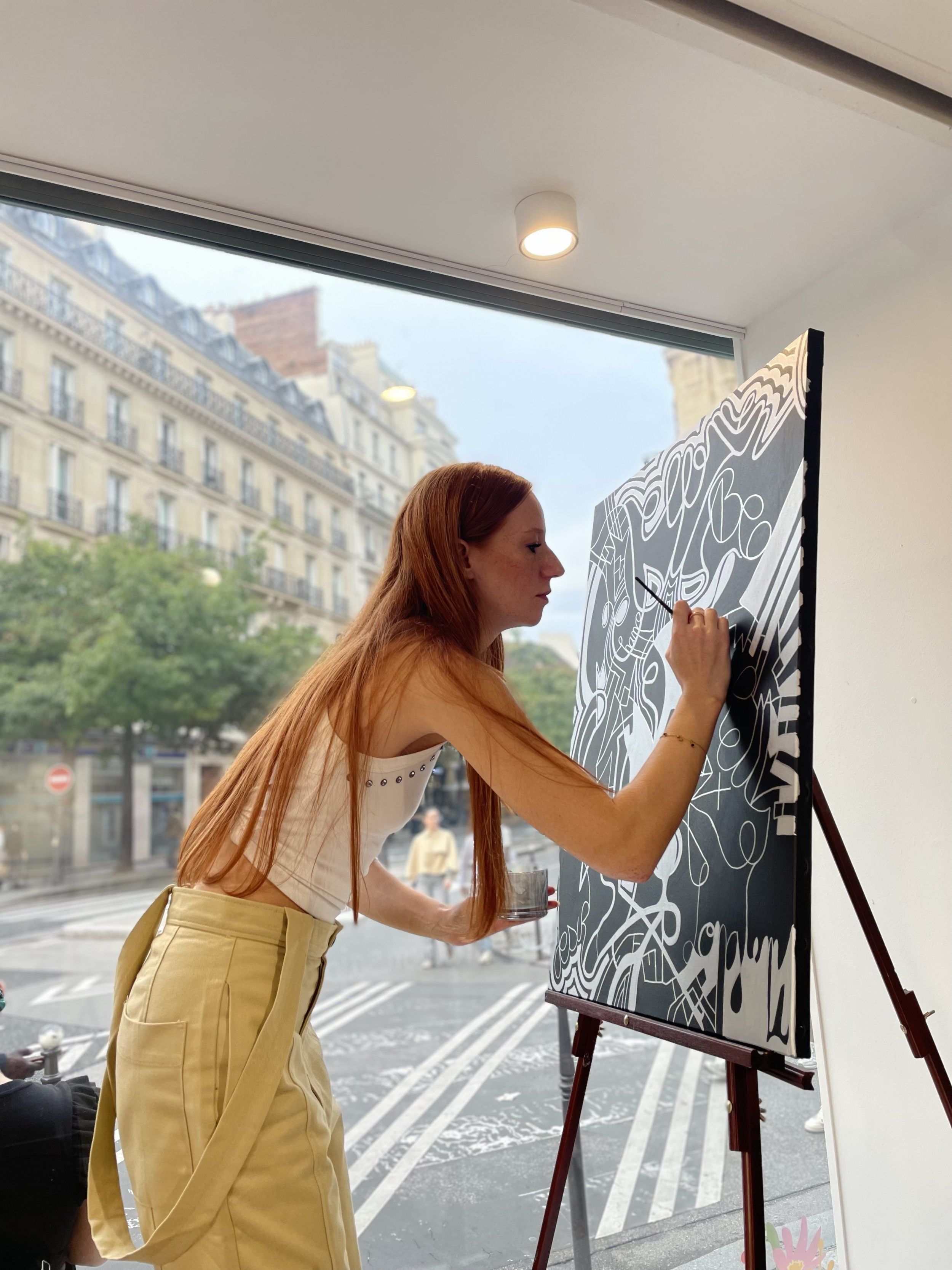 L'artiste peintre, Manon SAJOUS, qui peins dans la vitrine d'un pop up à Paris. Elle peint dans la vitrine.