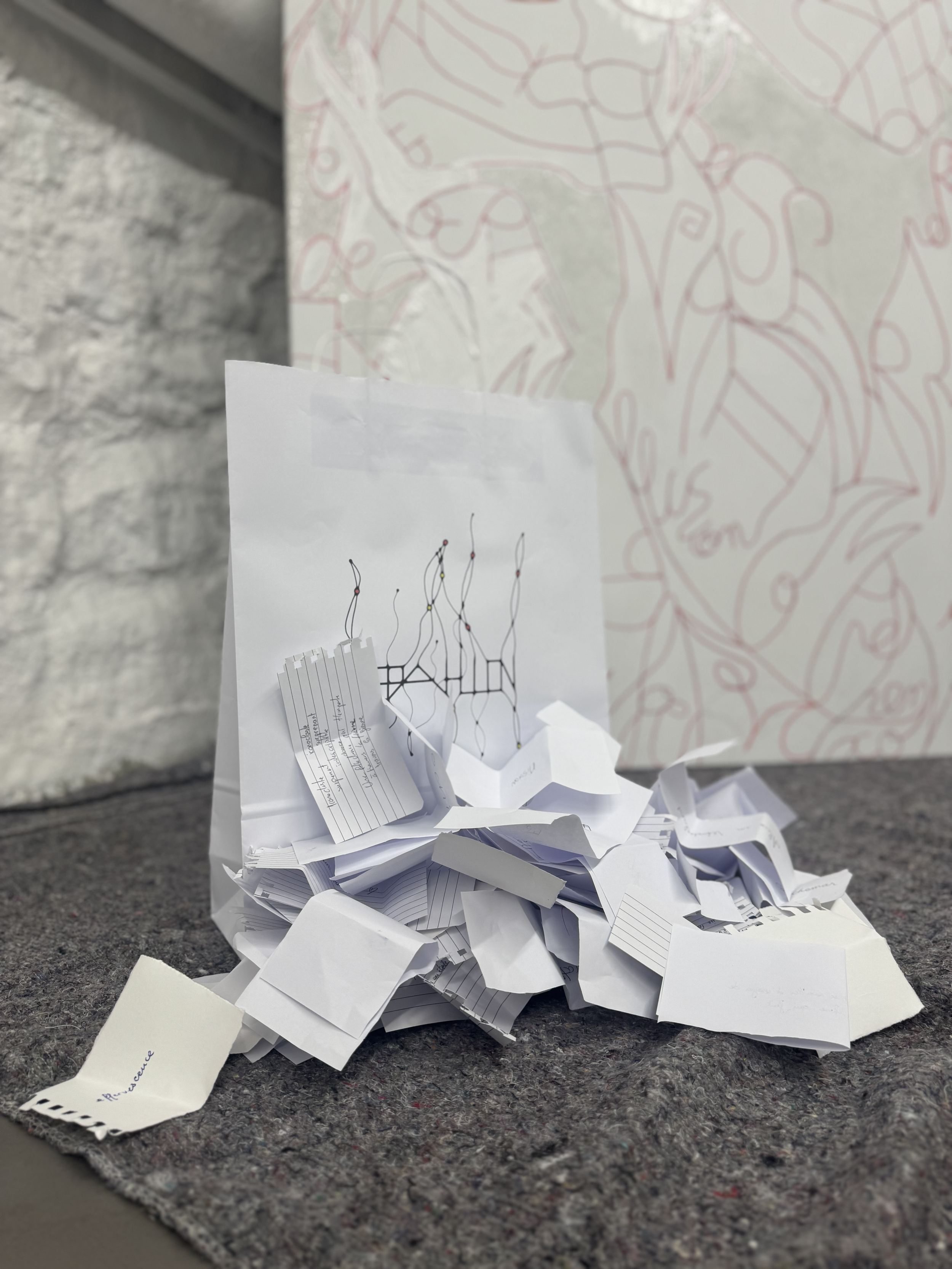 Un tas de papiers froissés avec des notes manuscrites et des dessins, placé sur un tapis, avec un mur en pierre en arrière-plan.