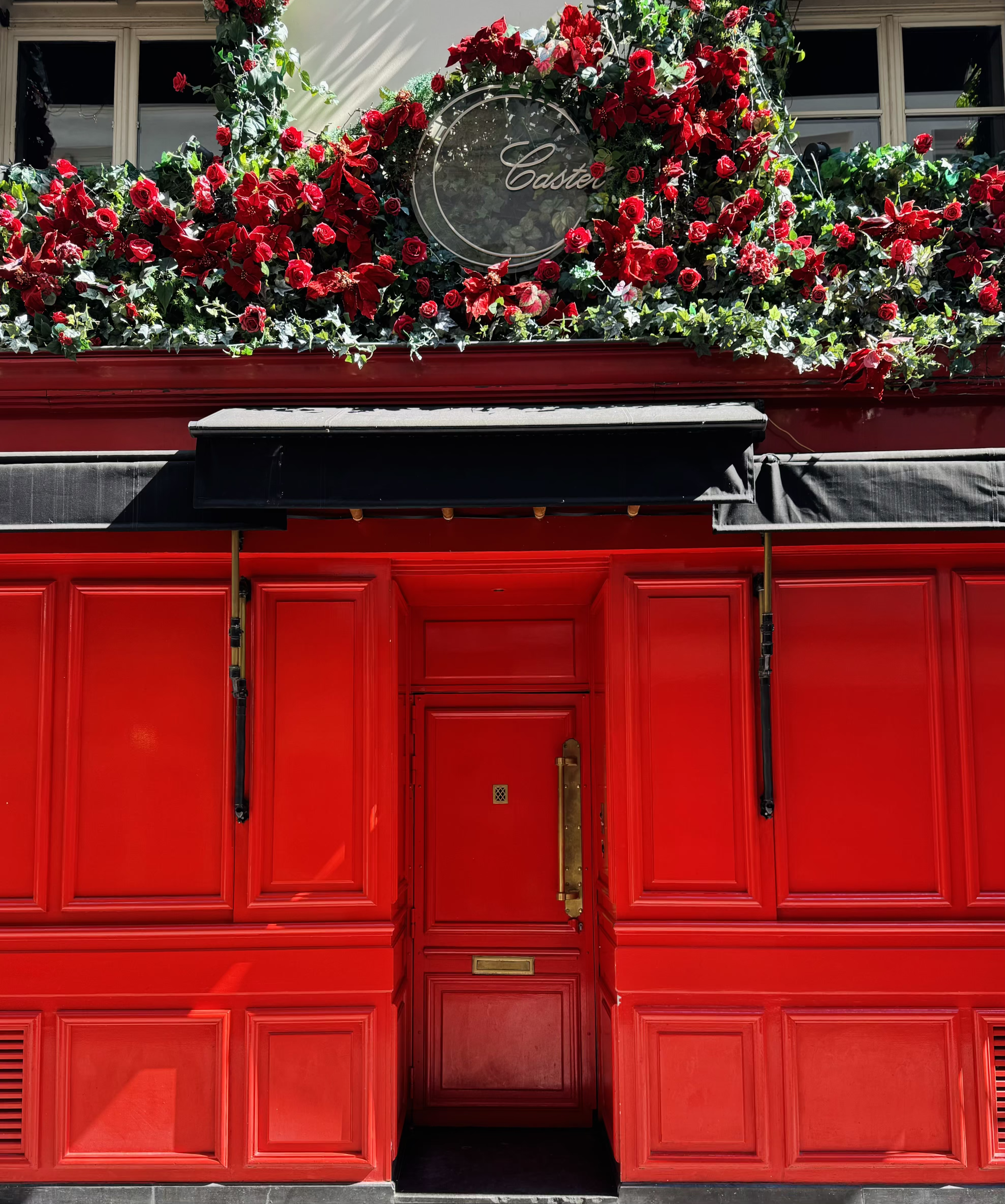 Une façade du Club privé "Castel" avec une porte centrale rouge entourée de fleurs rouges et de plantes décoratives, avec un panneau au-dessus portant le nom 'Castel'.