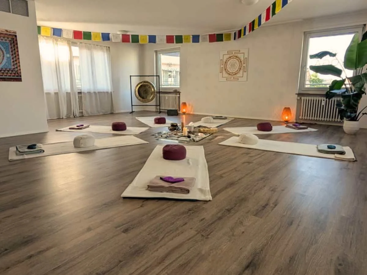 Raum für Breathwork. Dekoriert mit Meditationskissen, weissen Vorhängen, Dekorationsgegenstände wie Kerzen, Laternen und Vasen mit Blumen, Holzboden.