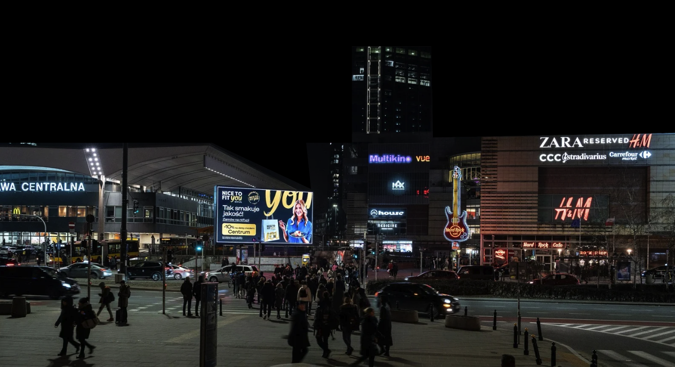 Reklama Urban Ads 'Nice To Fit You' na ekranie LED obok Złotych Tarasów i Hard Rock Cafe w Warszawie – nocna ekspozycja w centrum miasta