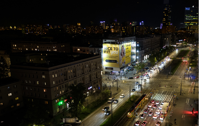Wielkoformatowa reklama Urban Ads 'Nice To Fit You' na elewacji budynku przy ul. Marszałkowskiej w Warszawie – nocna ekspozycja