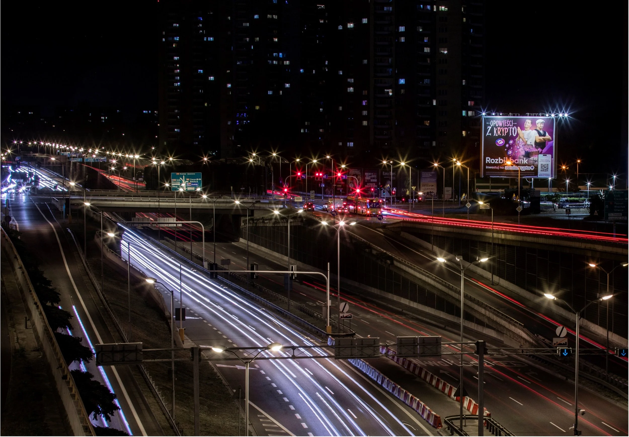 Reklama kampanii 'Z Krypto – Rozbij bank' na billboardzie przy głównej trasie w Warszawie – widok nocny z dynamicznym ruchem
