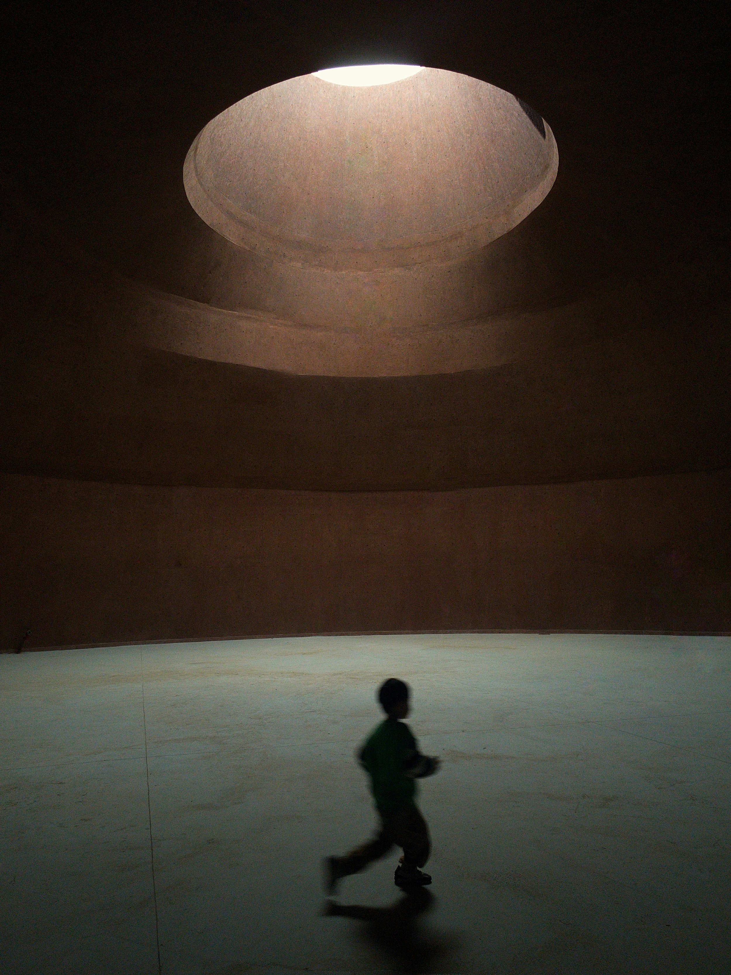 Silhouette of a young boy running inside a structure with a circular opening at the top, allowing light to enter.