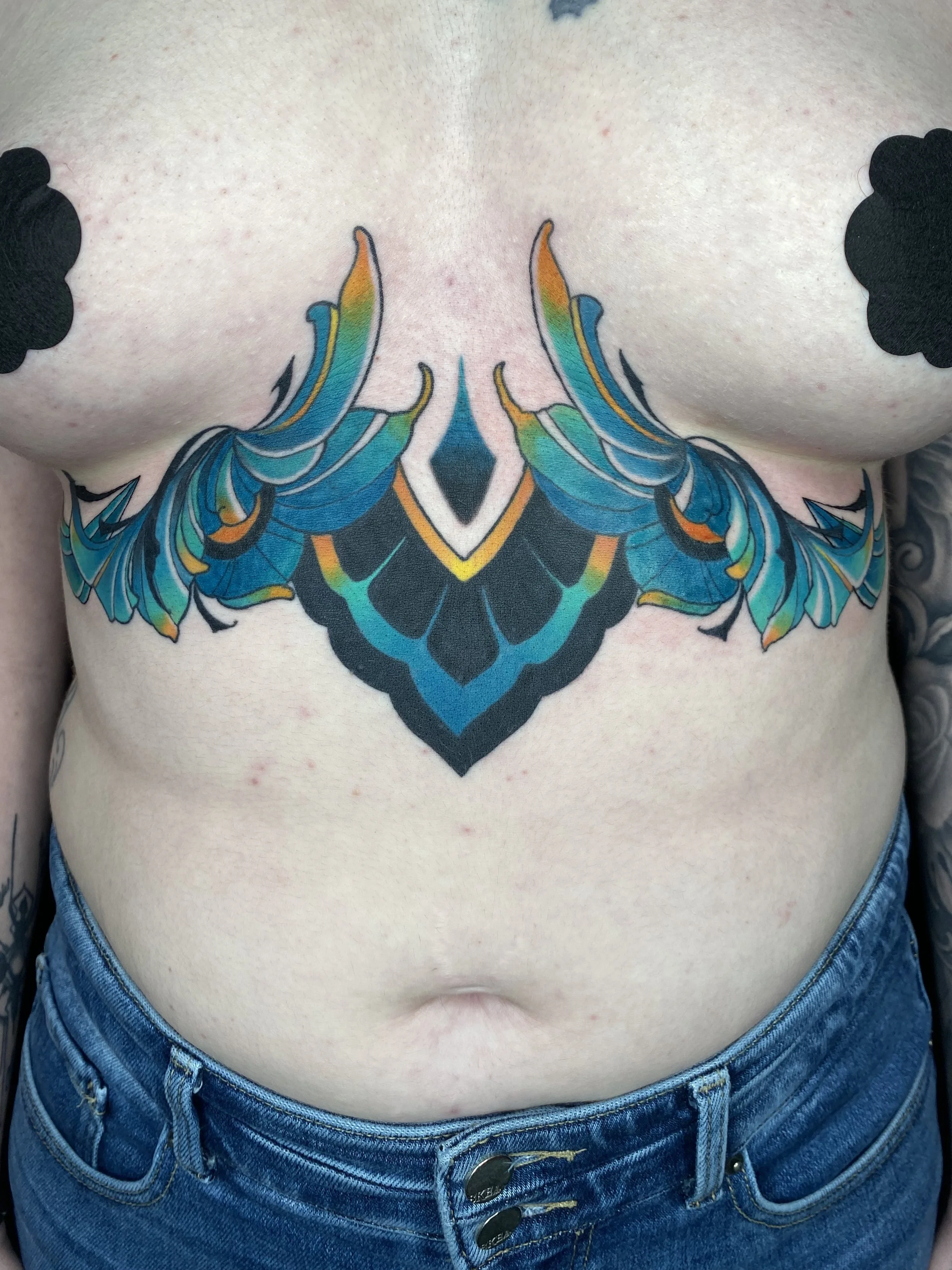 American Traditional-inspired ornamental underbust tattoo with vivid color by Denver tattoo artist Joshua Socrates in RiNo.
