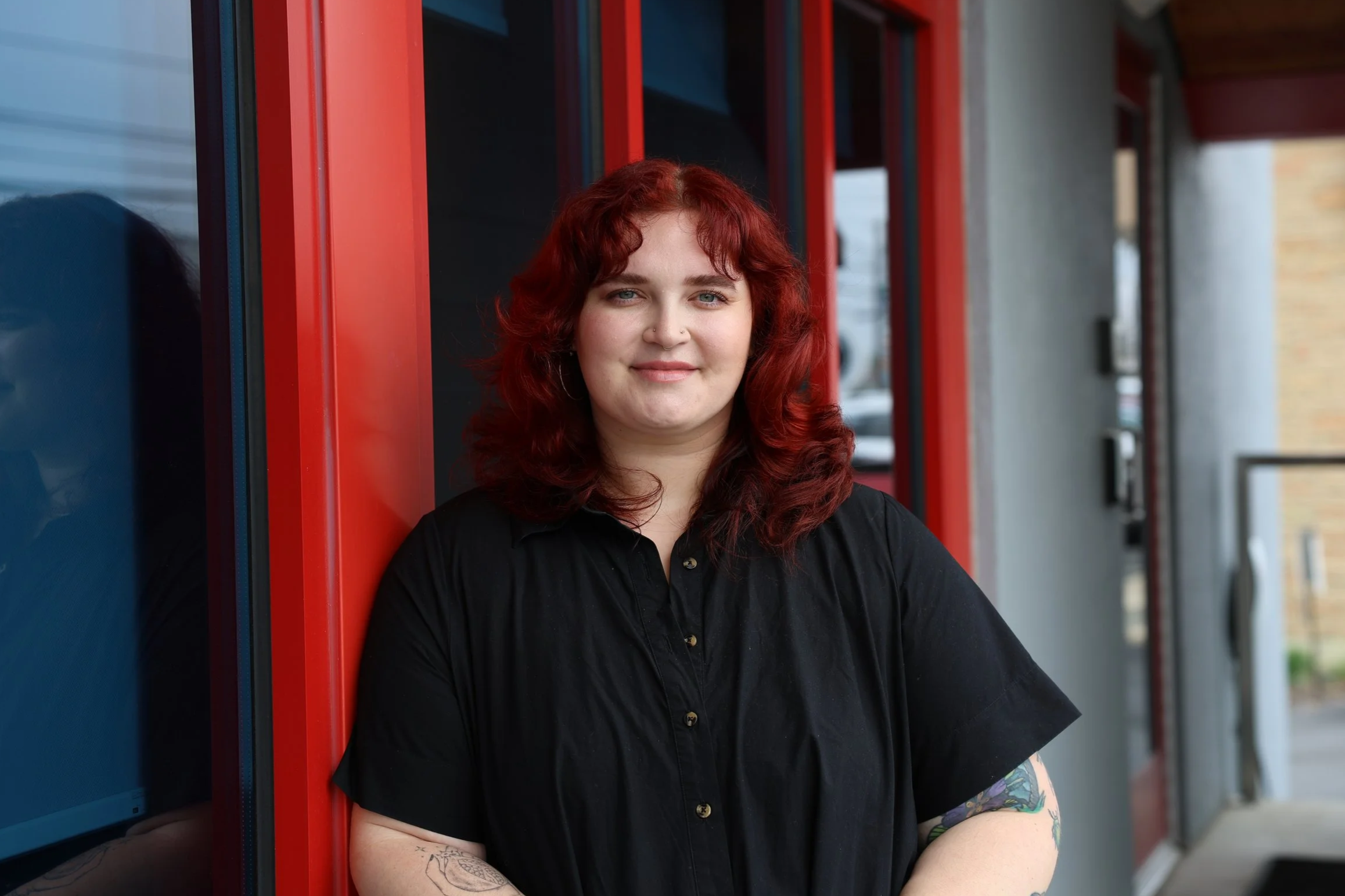 A woman with red hair standing in front of a window with a red frame and metal bars.