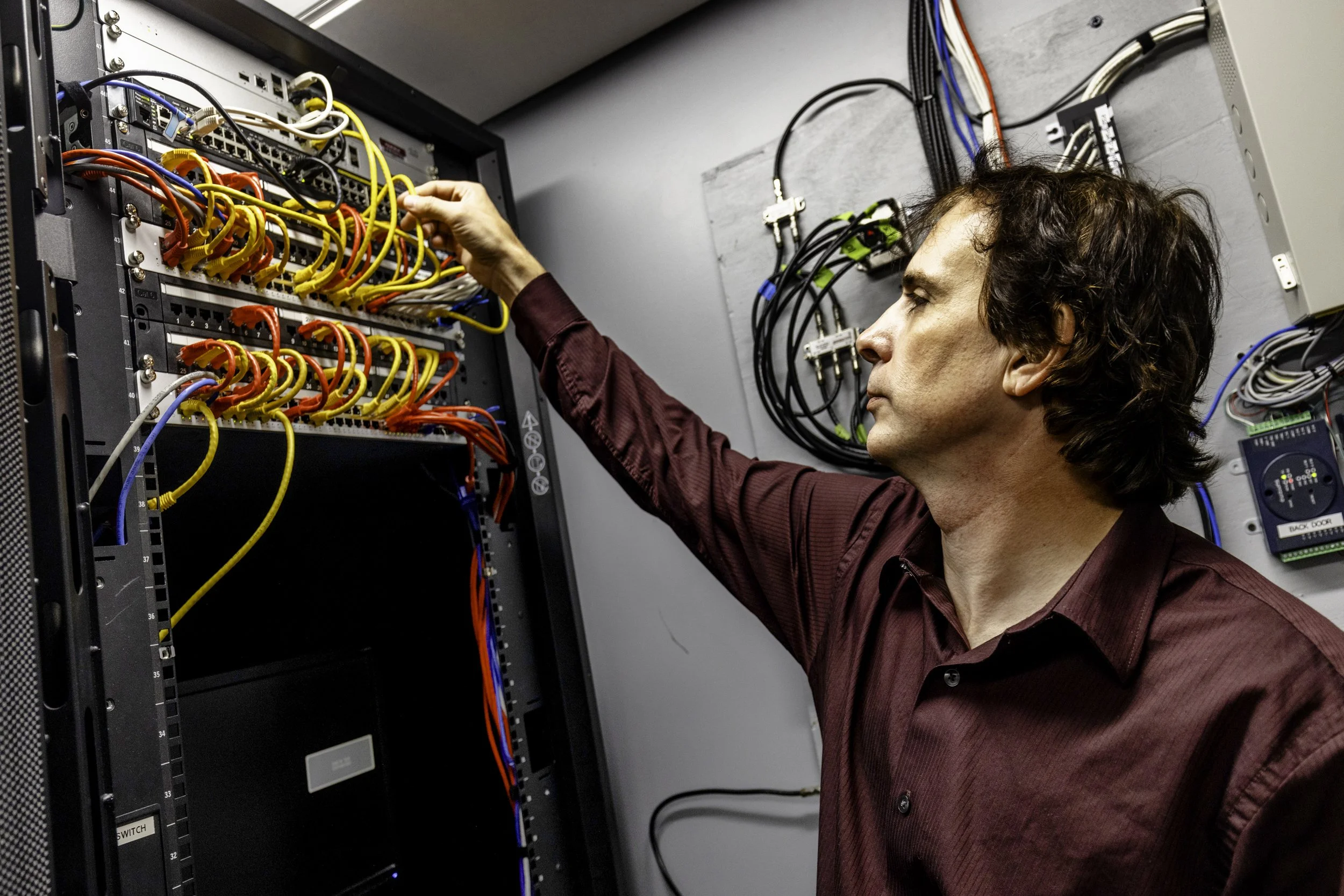 A man in a plaid shirt working inside a server room, connecting or adjusting network cables in a server rack.