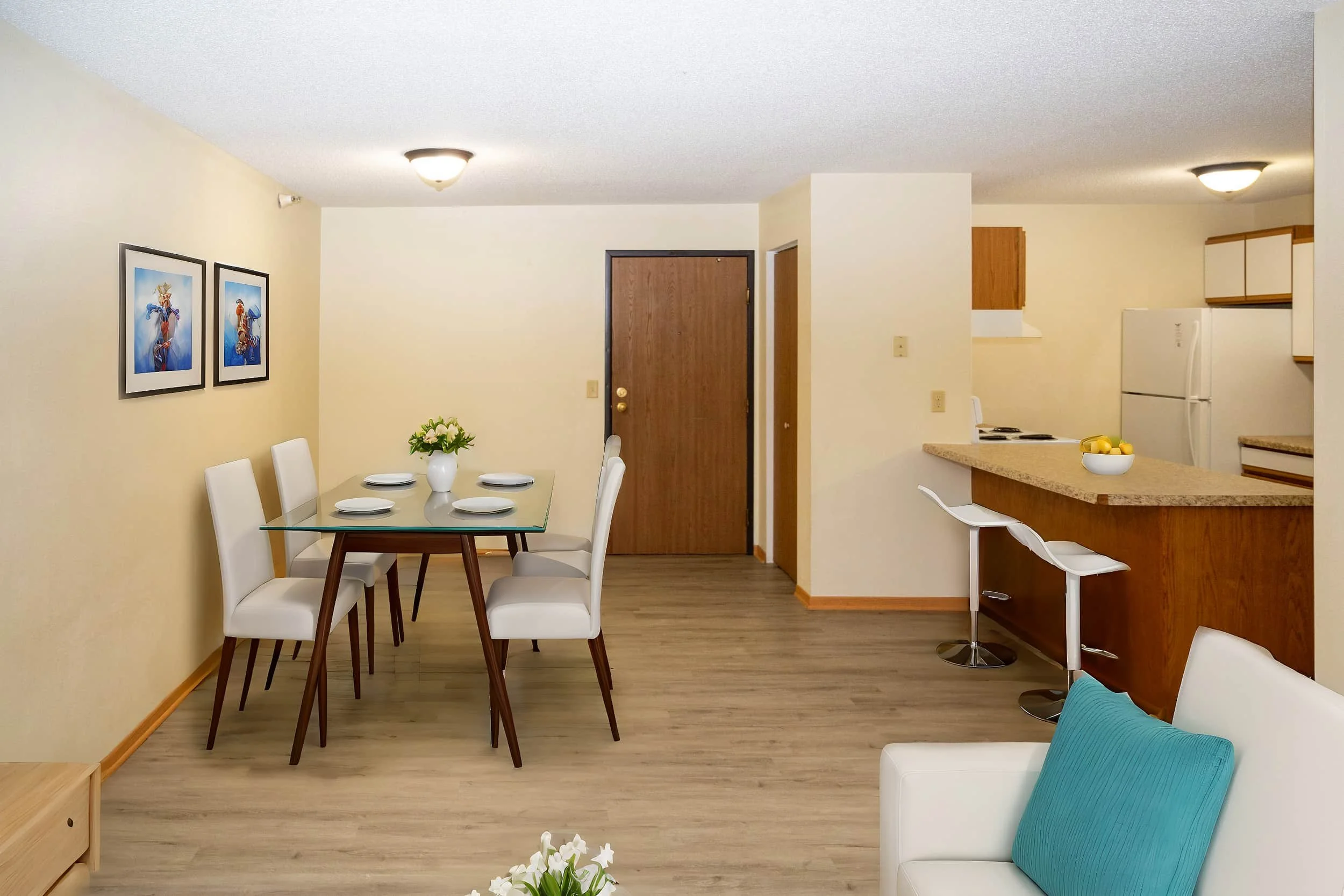Modern apartments in Rochester feature a dining and kitchen area with a glass table, white chairs, barstools, and neutral colors.
