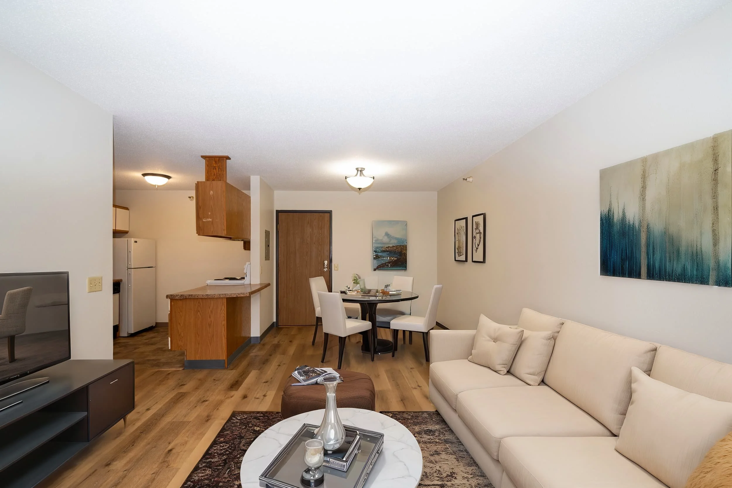 A modern apartments in Rochester living room with a beige sofa, round coffee table, dining area, and open kitchen with wood accents.