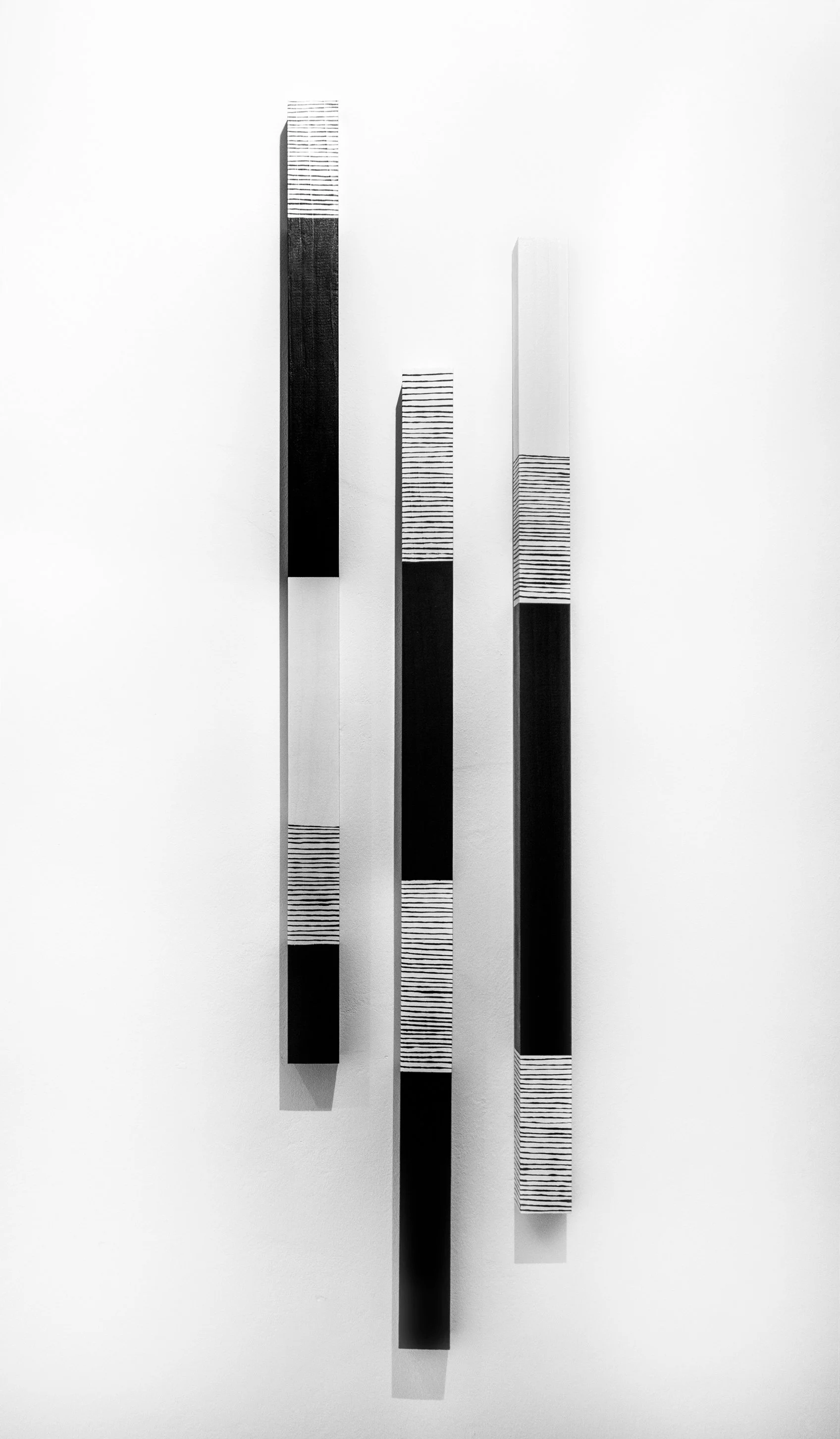 Abstract black and white striped vertical artwork on a wall, with three rectangular panels of varying heights and designs.