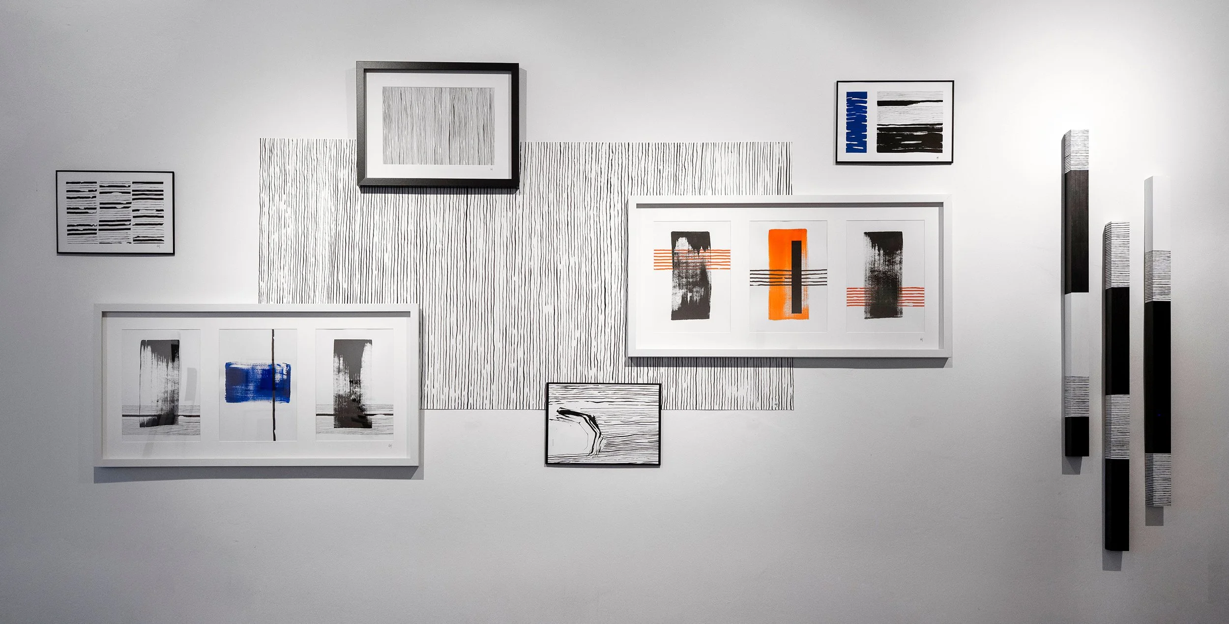 Gallery wall with abstract black, white, orange, and blue artwork, arranged with various frames and textures.
