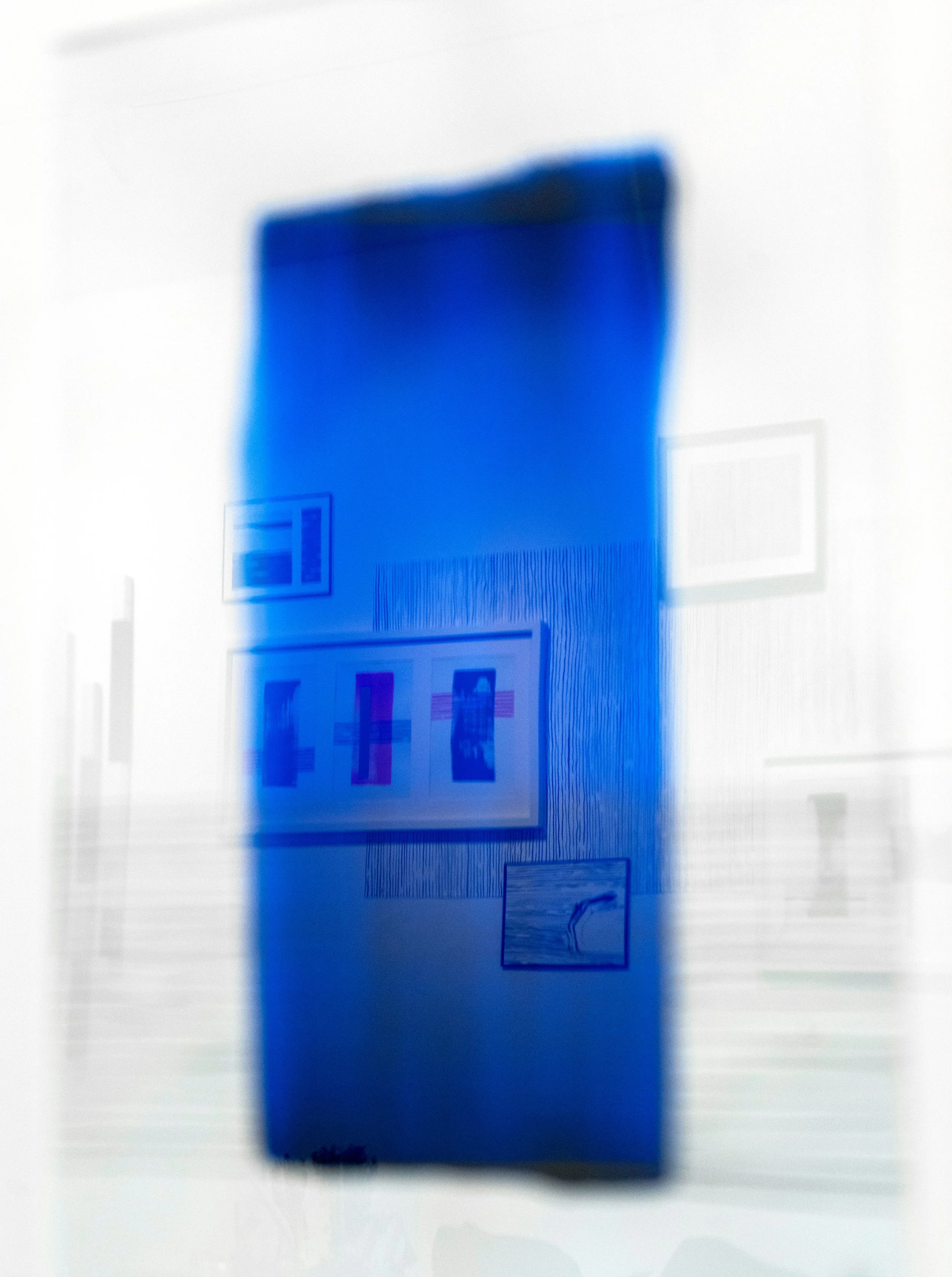 Blurred photo of an interior wall with framed artwork and a small picture, illuminated with a blue hue.