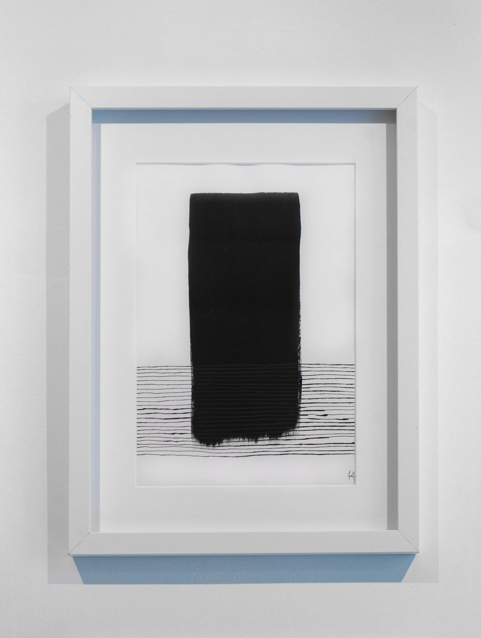 Minimalist black and white abstract art featuring a tall black rectangular shape with horizontal lines beneath it, framed in white and mounted on a white wall.