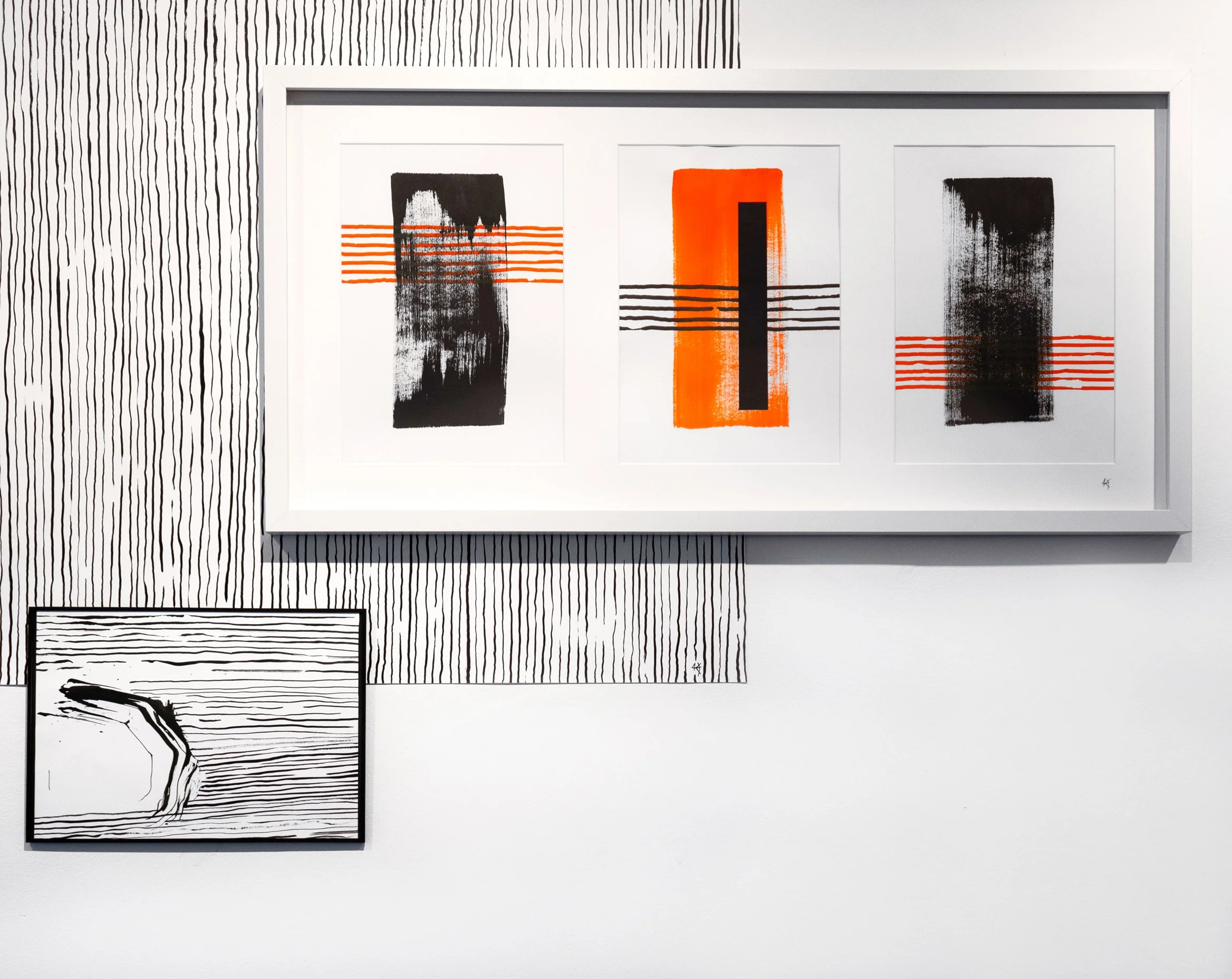 Triptych abstract art with black and orange rectangular shapes and horizontal lines, and a black and white line drawing of a hand on the wall.