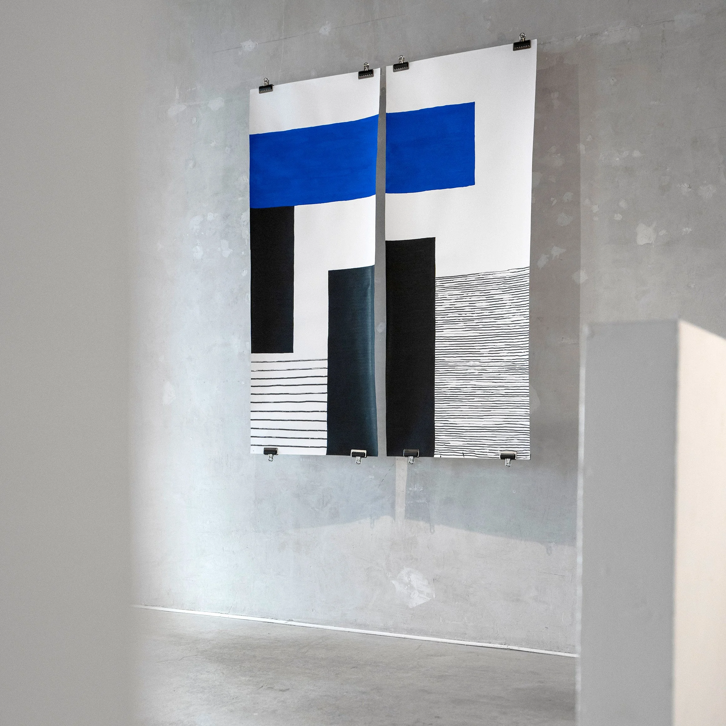 Deux grandes œuvres d'art modernes accrochées à un mur gris, composées de formes géométriques avec des lignes horizontales noires et blanches, et des blocs de couleur bleue et noire.