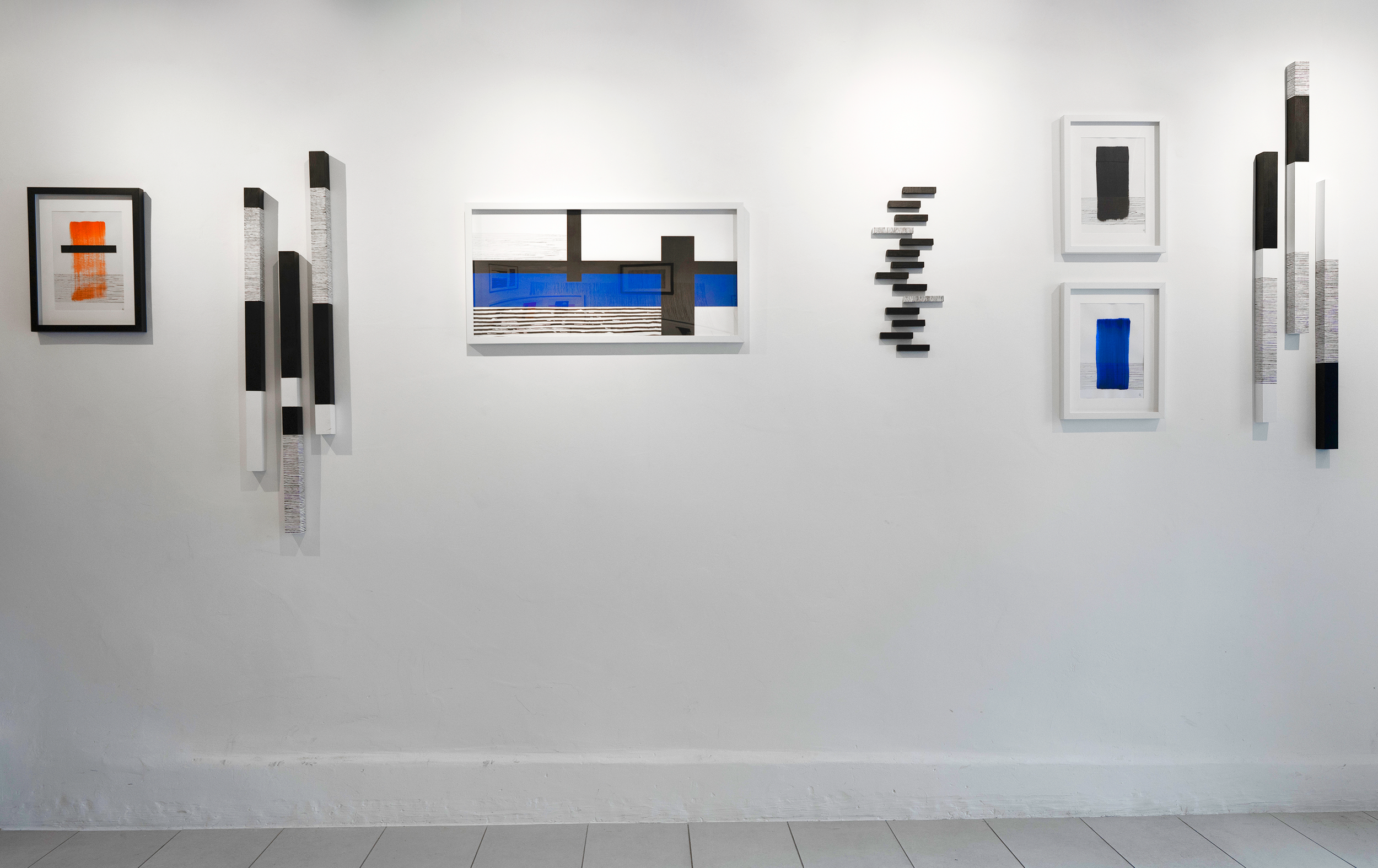 Art gallery wall displaying abstract paintings and mixed media artwork with geometric shapes and bold colors.