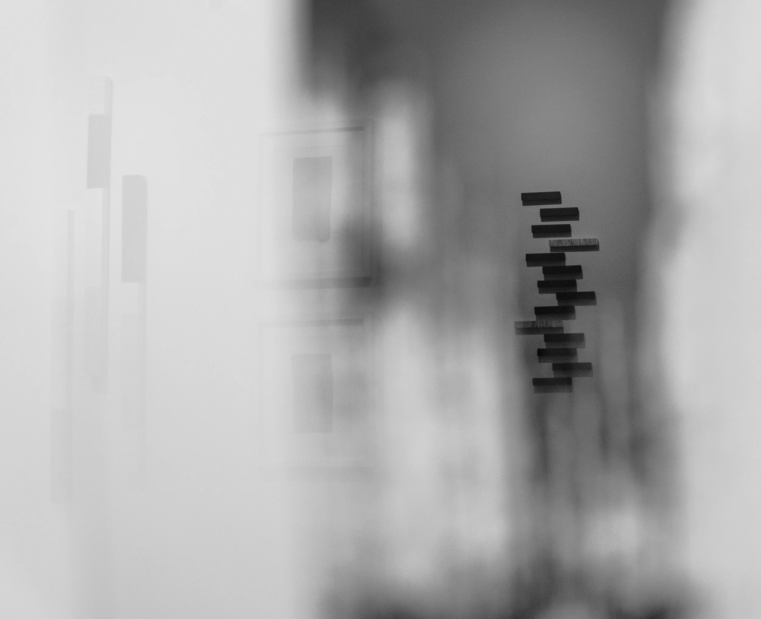 Black and white image of an art gallery wall with artwork and a tall, vertical structure made of small rectangular blocks.