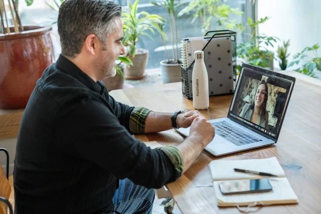 man at desk looking at laptop for a zoom call with a woman