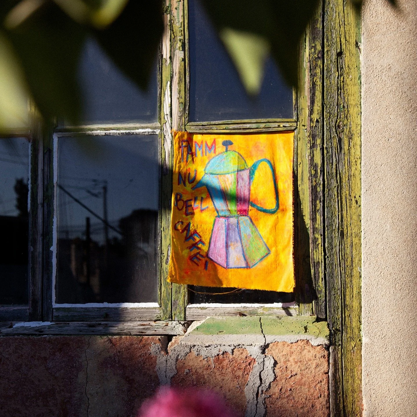 Tableau accroch&eacute; &agrave; la vitre d&rsquo;une maison fatigu&eacute;e o&ugrave; la peinture s&rsquo;effrite comme des souvenirs perdus. Une cafeti&egrave;re arc‑en‑ciel y souffle &laquo; Famm nu bell caff&egrave; &raquo; et la fen&ecirc;tre se