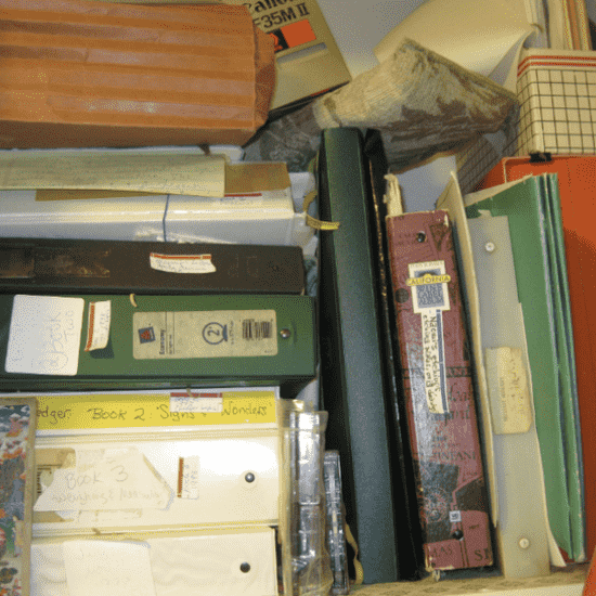 A closet shelf crowded with binders, folders, and manuscript boxes representing a book in progress..