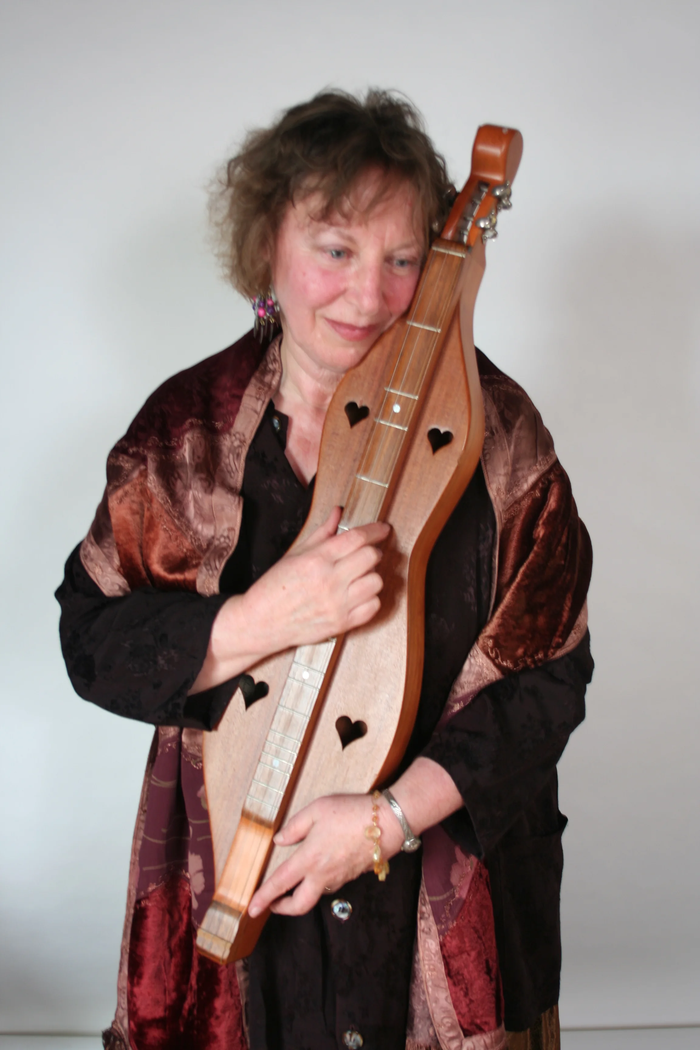 Naomi Rose cradling a mountain dulcimer against her shoulder, eyes lowered, wearing a dark patterned velvet shawl.