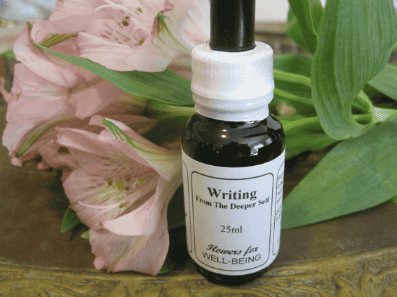 A small black dropper bottle labeled 'Writing From The Deeper Self, 25ml, Flowers for WELL-BEING,' placed beside pink flowers and green leaves on a wooden surface.