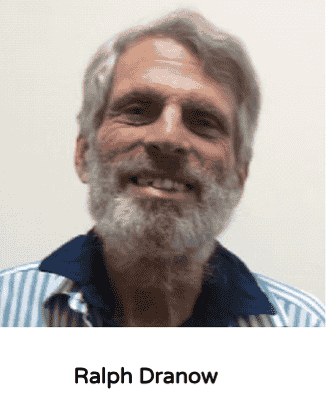 A smiling man with gray hair and a beard wearing a striped shirt and dark collar.