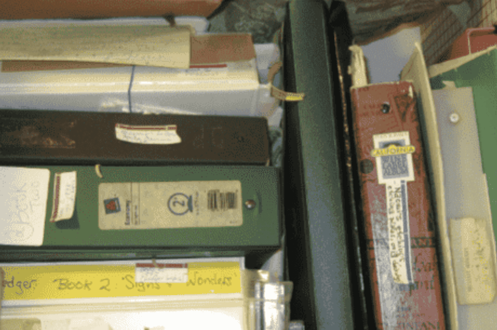 A closet shelf crowded with binders, folders, and manuscript boxes — some hand-labeled “Book 2,'” “Book 3” — representing writing projects stored away and forgotten.