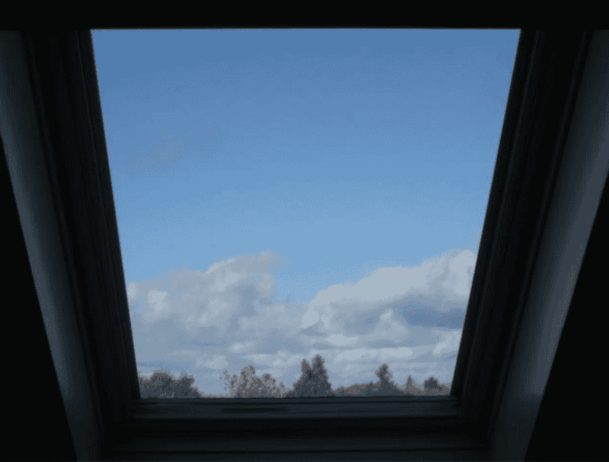 View through a skylight window showing blue sky with white clouds and trees on the horizon, illustrating the concept of “Something from Nothing” in the creative process