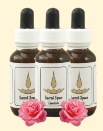 Three Sacred Space Essentials flower-essence dropper bottles standing together, with pink roses in front.