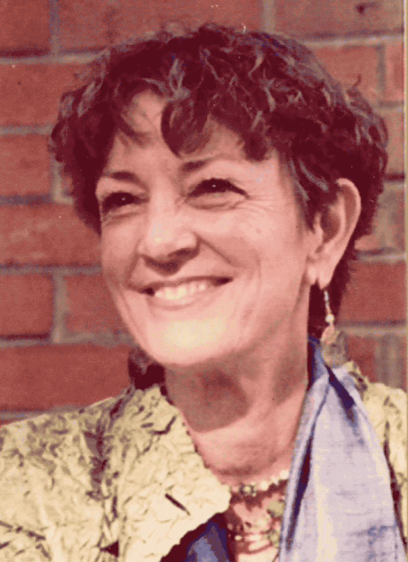 Risala Mary Laird, artist and spiritual teacher, smiling, before a brick wall.