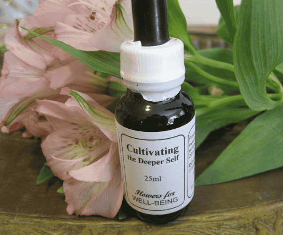 A small black dropper bottle labeled "Cultivating the Deeper Self" with a white cap, placed among pink flowers and green leaves.
