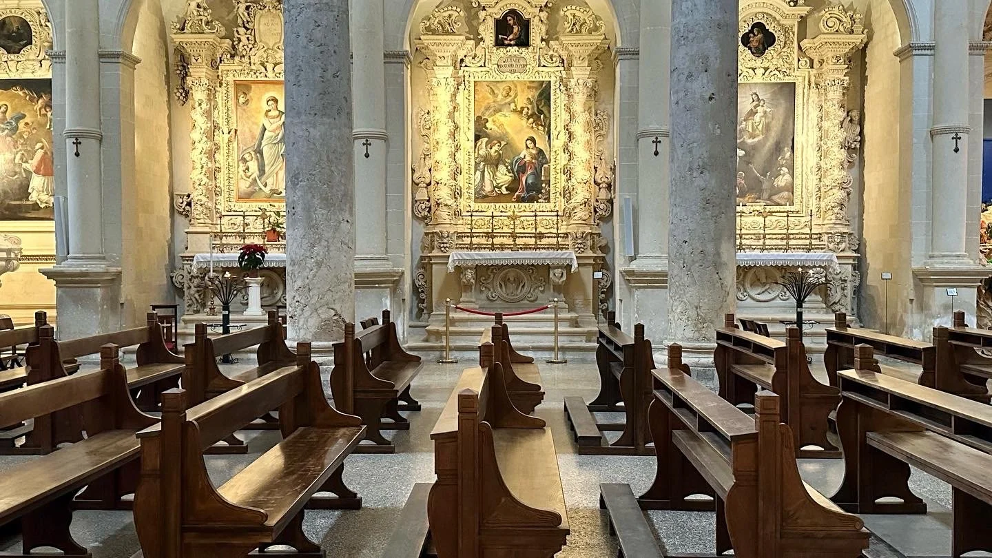 Interior of a church with wooden pews, marble columns, and ornate religious paintings and sculptures on the altar.