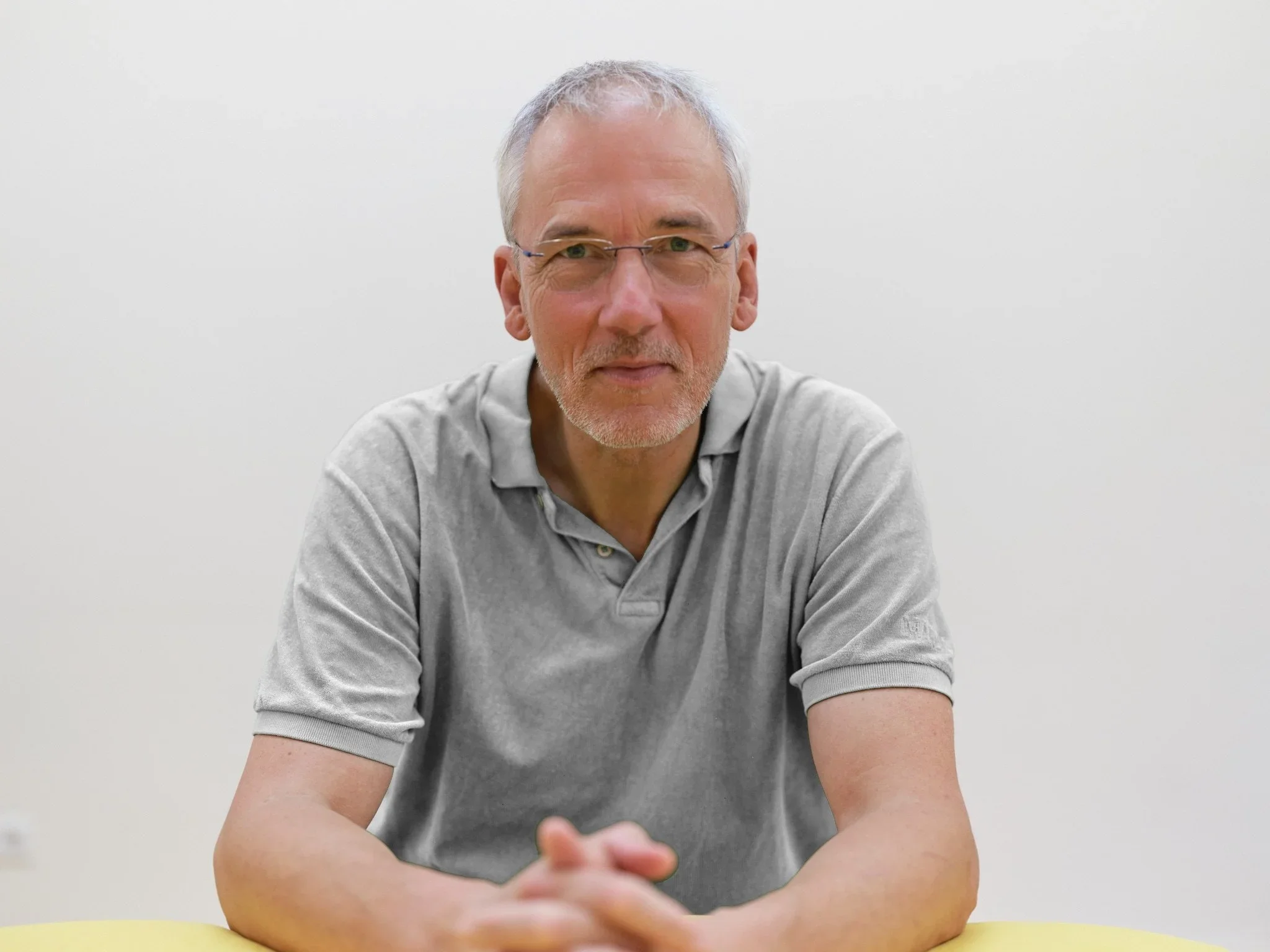 Andreas Brieschke sitzt an einem Tisch vor einer weißen Wand und schaut in die Kamera.