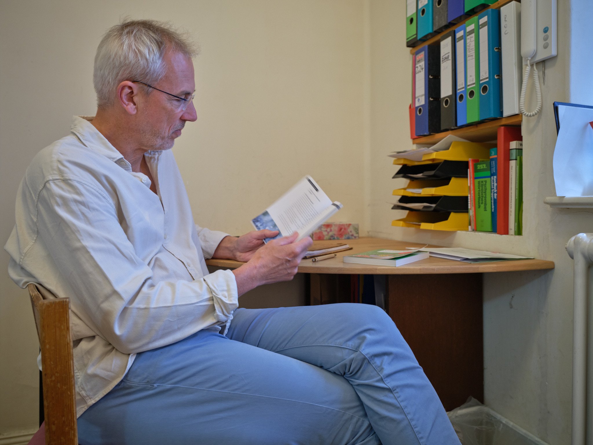 Andreas Brieschke sitzt in der Teeküche seiner Praxis und blättert in seinem Buch über Naturheilkunde und Viruserkraknungen