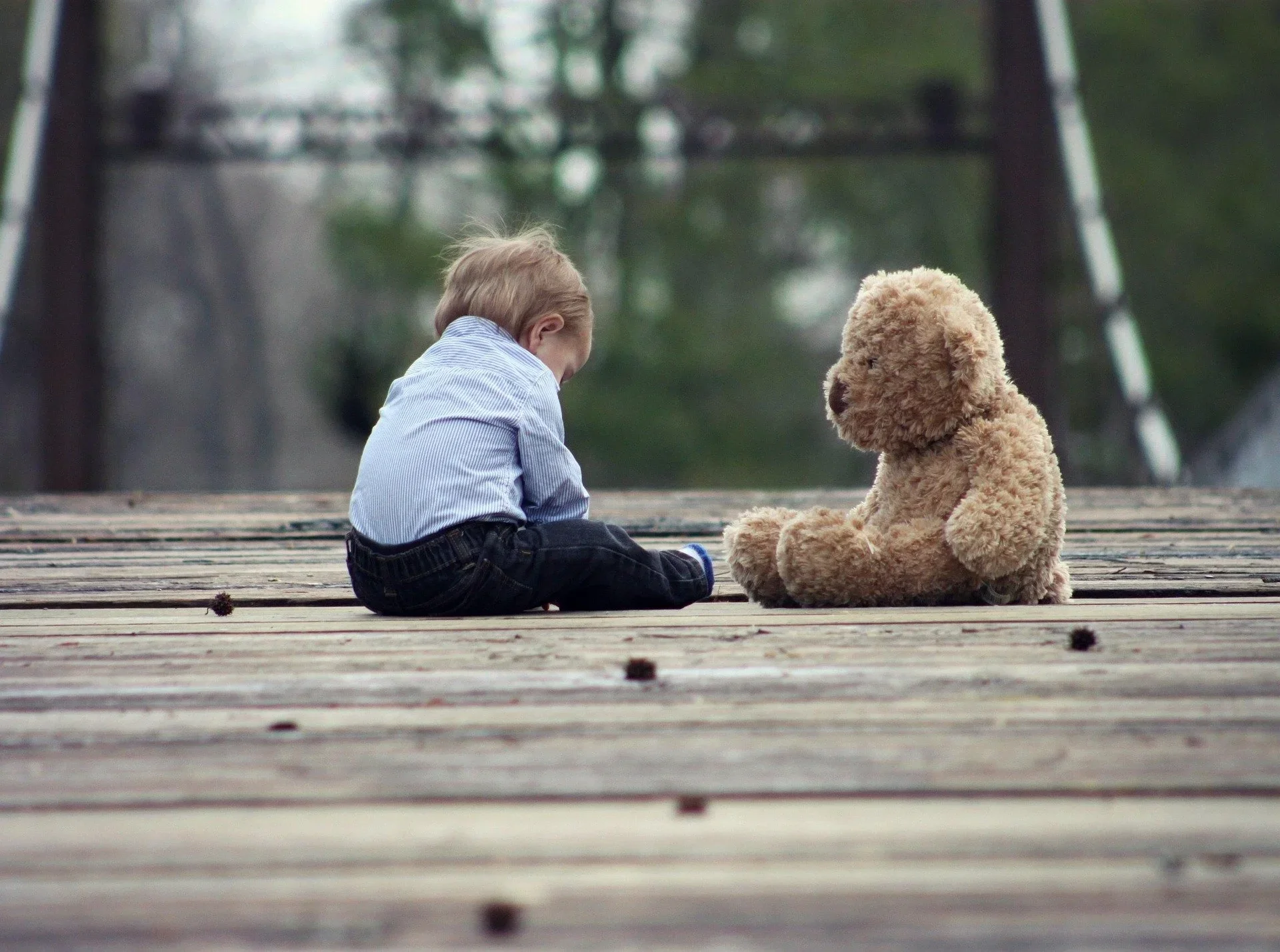 Kleiner Junge spielt versunken auf dem Boden, neben ihm ein Teddybär.