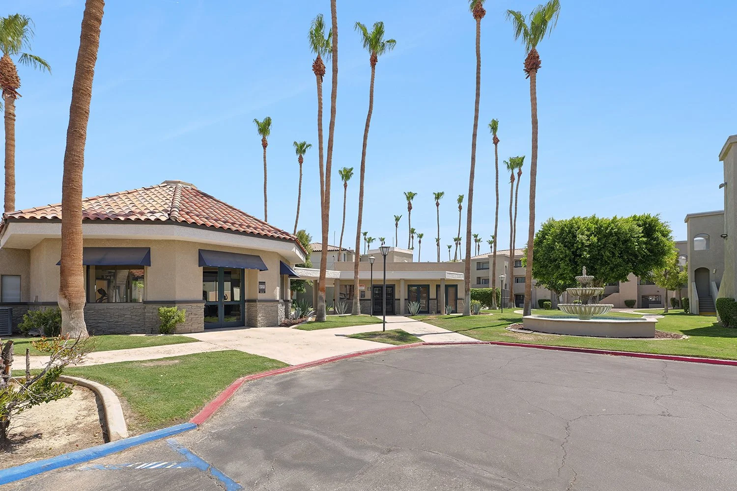 An image capturing a well-manicured, open courtyard in an apartment complex, featuring the leasing office. 