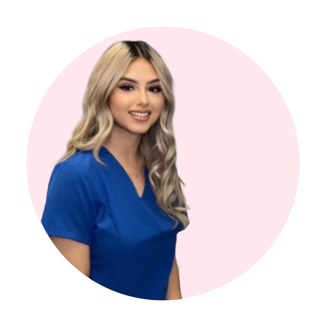 Young woman with blonde wavy hair wearing a blue medical scrubs smiling against a light pink circular background.