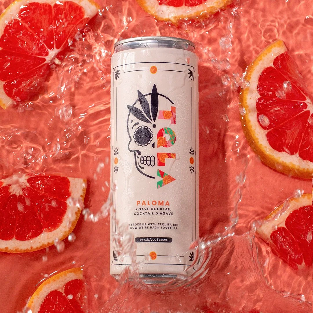 A can of Paloma agave cocktail surrounded by grapefruit and lemon slices with water splashing around.