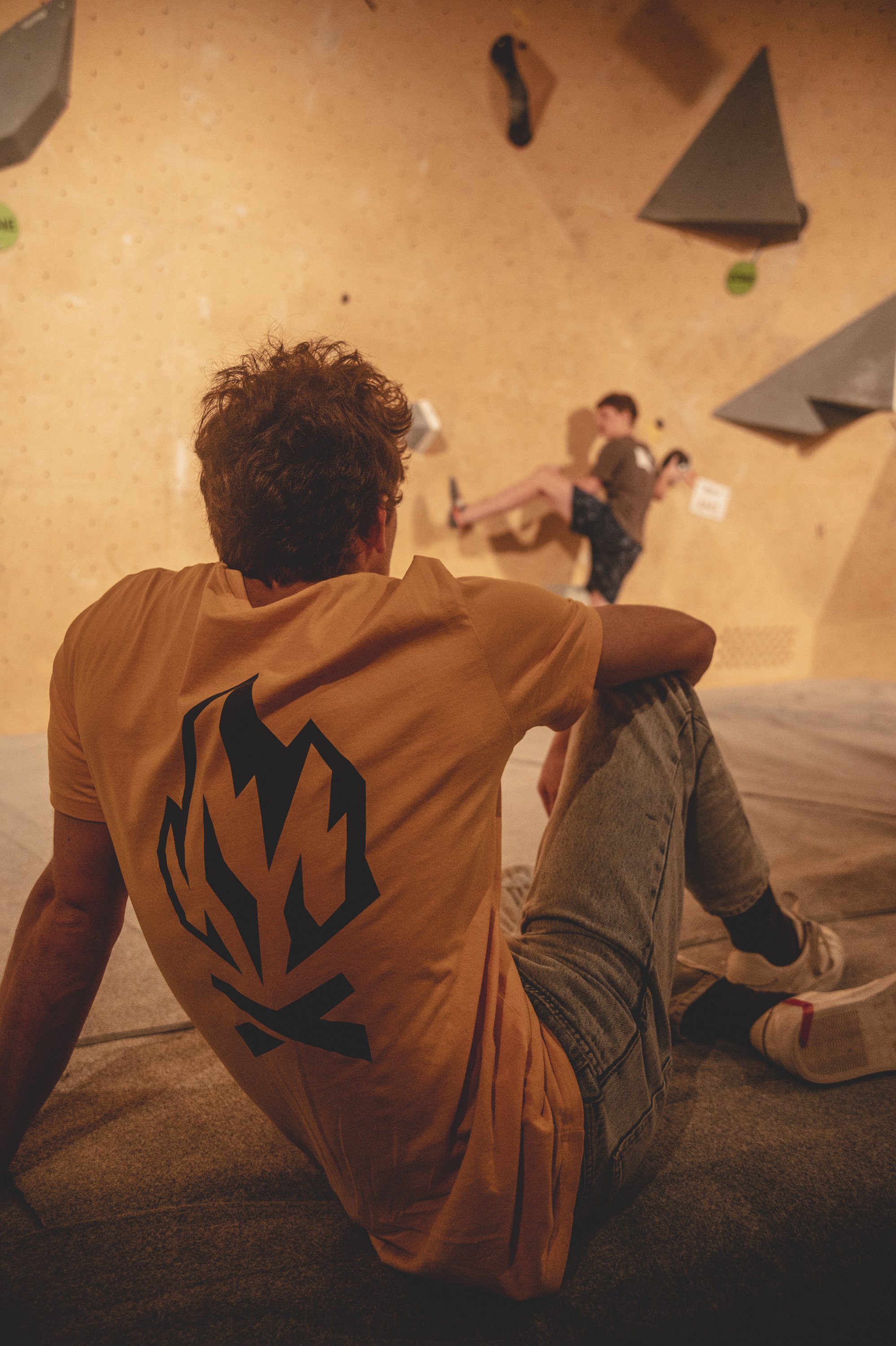 L'escalade de bloc est un sport qui captive autant les athlètes que les spectateurs. Sur cette photo, Julien Mathy nous offre une perspective unique : le regard d'un spectateur, absorbé par la performance d'un jeune grimpeur en pleine action lors de