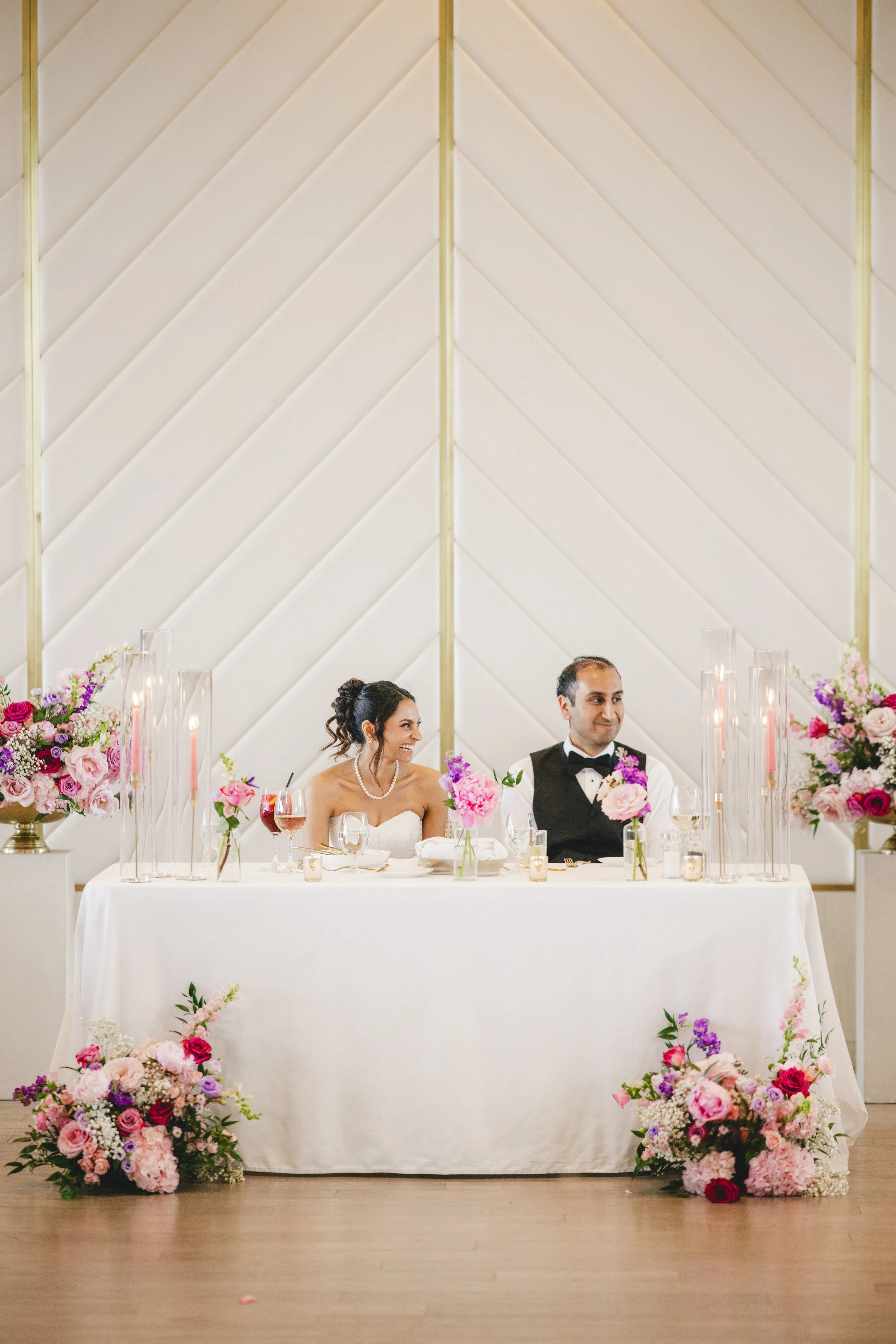 Pink and purple floral sweetheart tables with gold compotes and taper candles at a Pearle Hotel and Spa wedding reception.